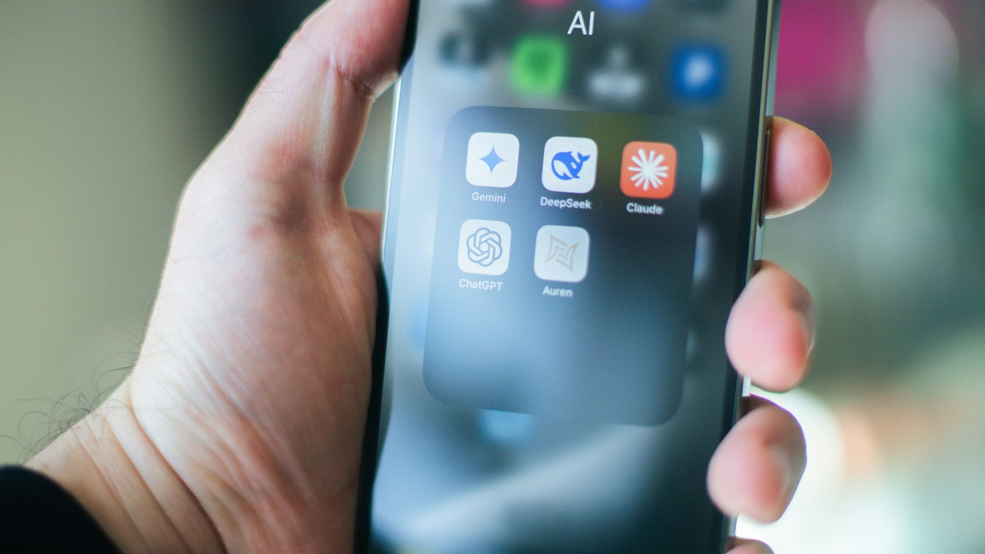 A hand holds a smartphone with various apps.