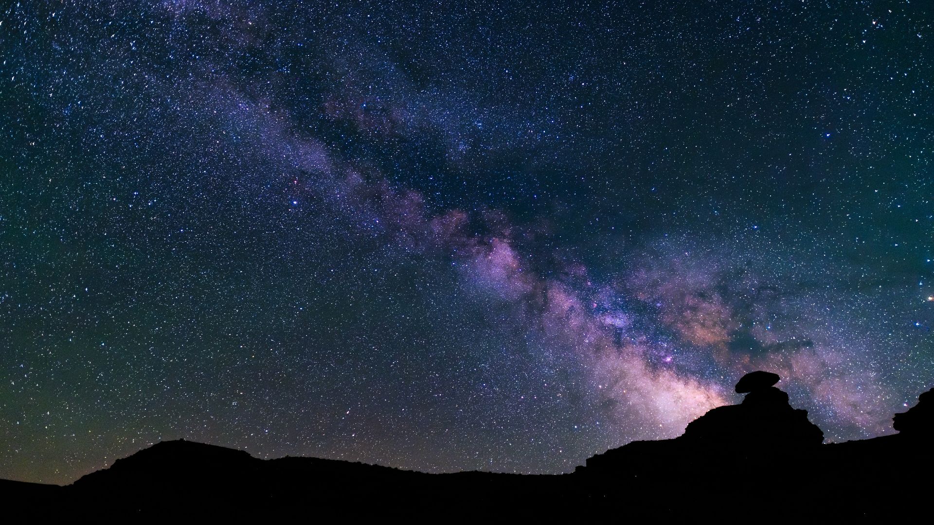 a person standing on top of a hill under a night sky filled with stars