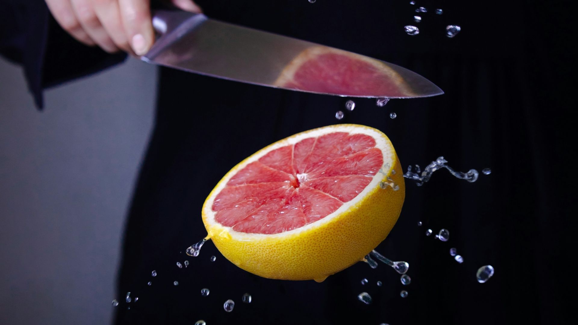 a person cutting a grapefruit with a knife