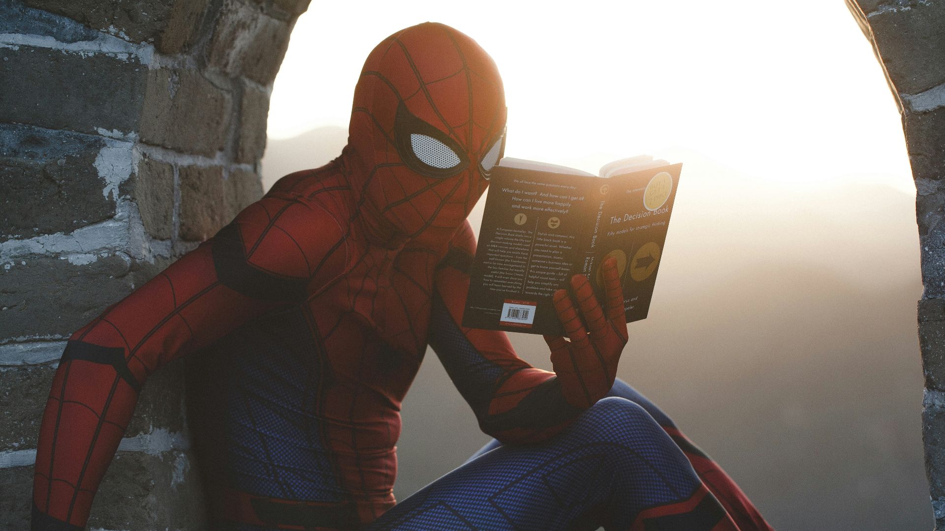 Spider-Man leaning on concrete brick while reading book