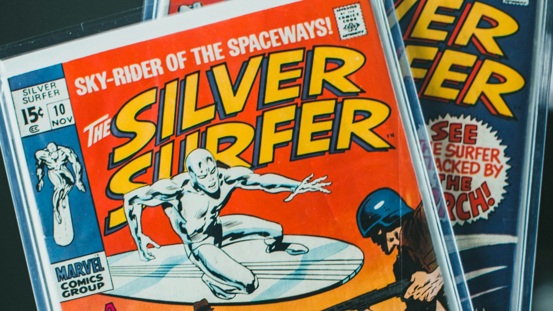 a person holding up two silver surfer comics