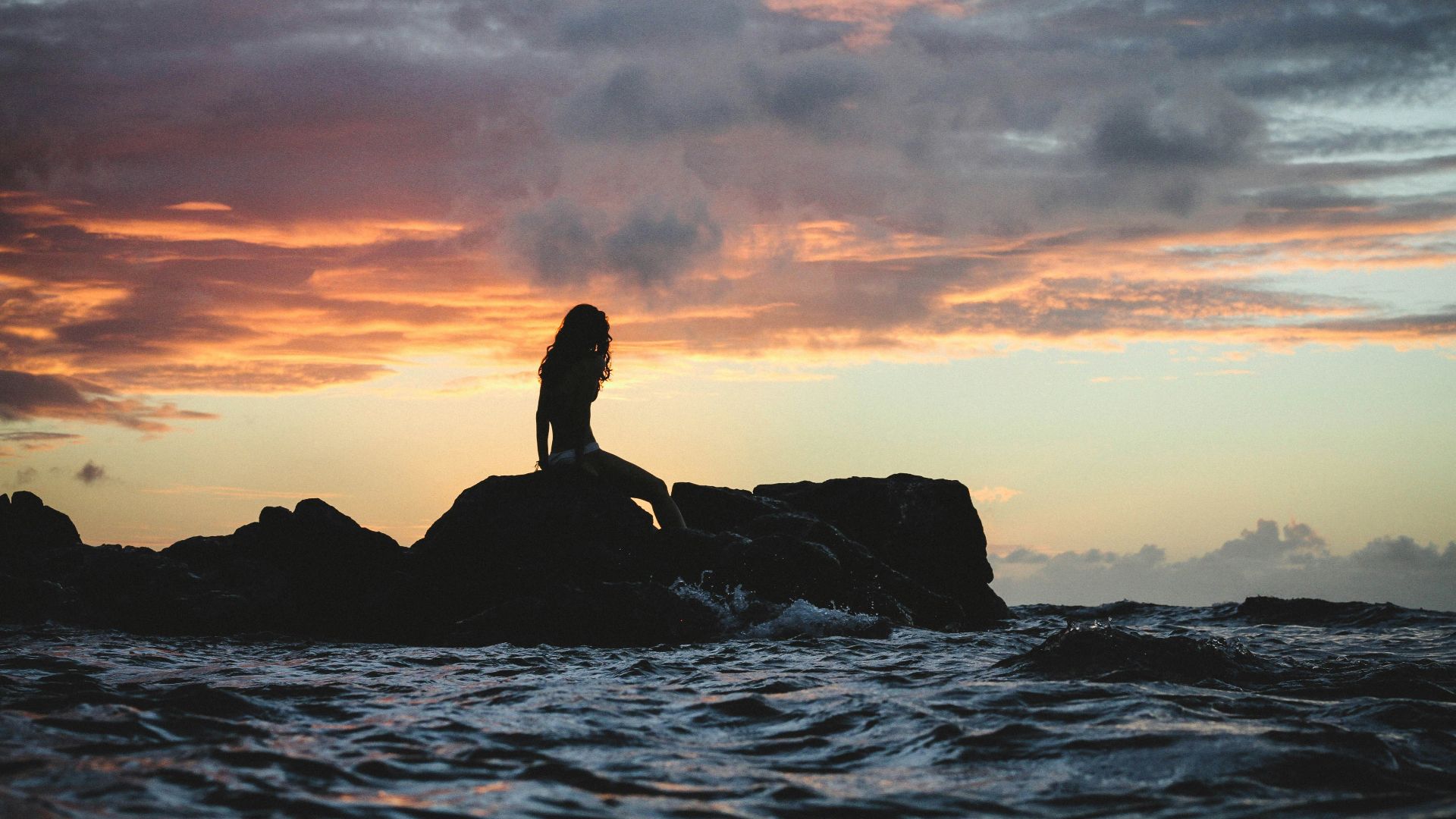 silhouette photo of woman sitting on rock during golden hour