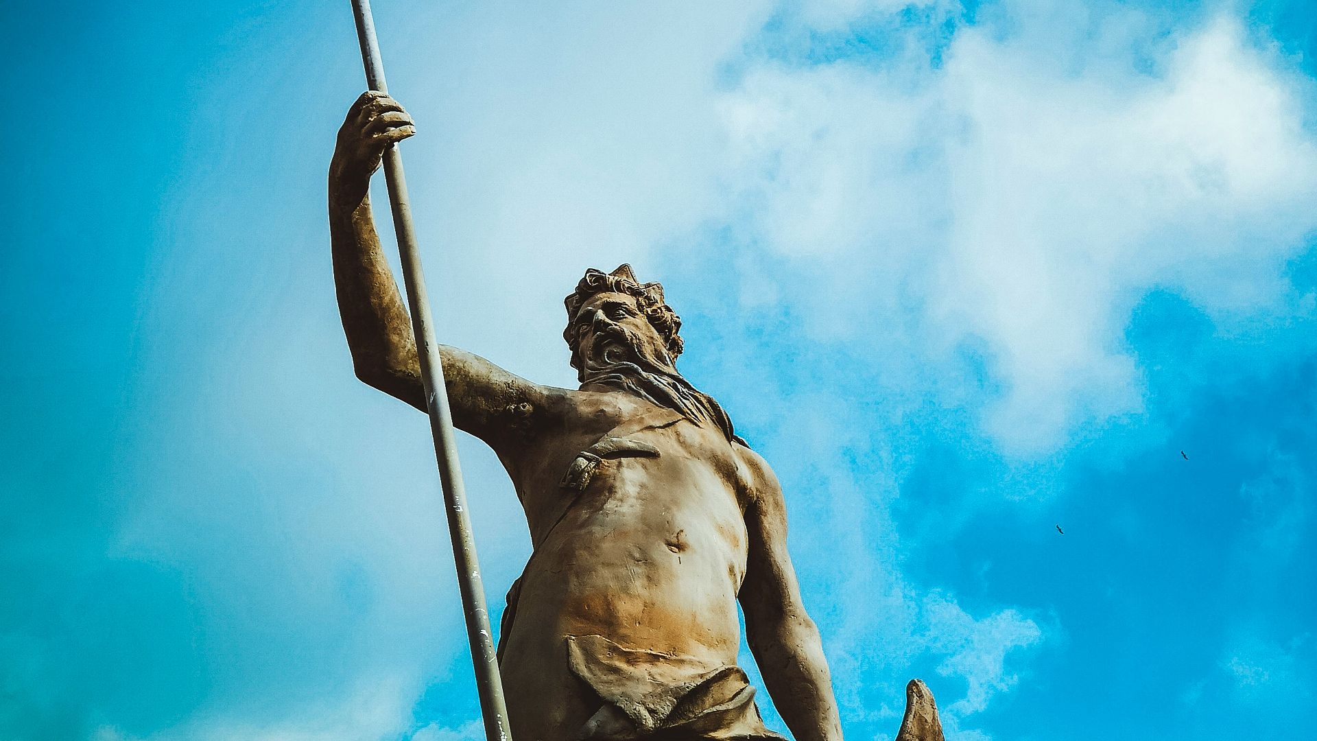 man holding trident statue under white clouds at daytime