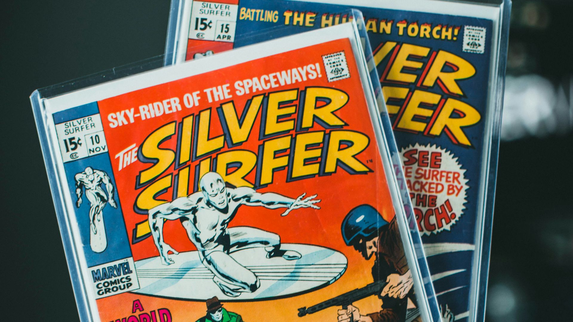 a person holding up two silver surfer comics