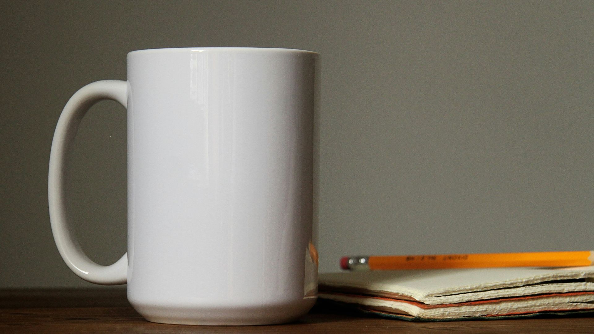 white ceramic mug beside orange pencil on open book page