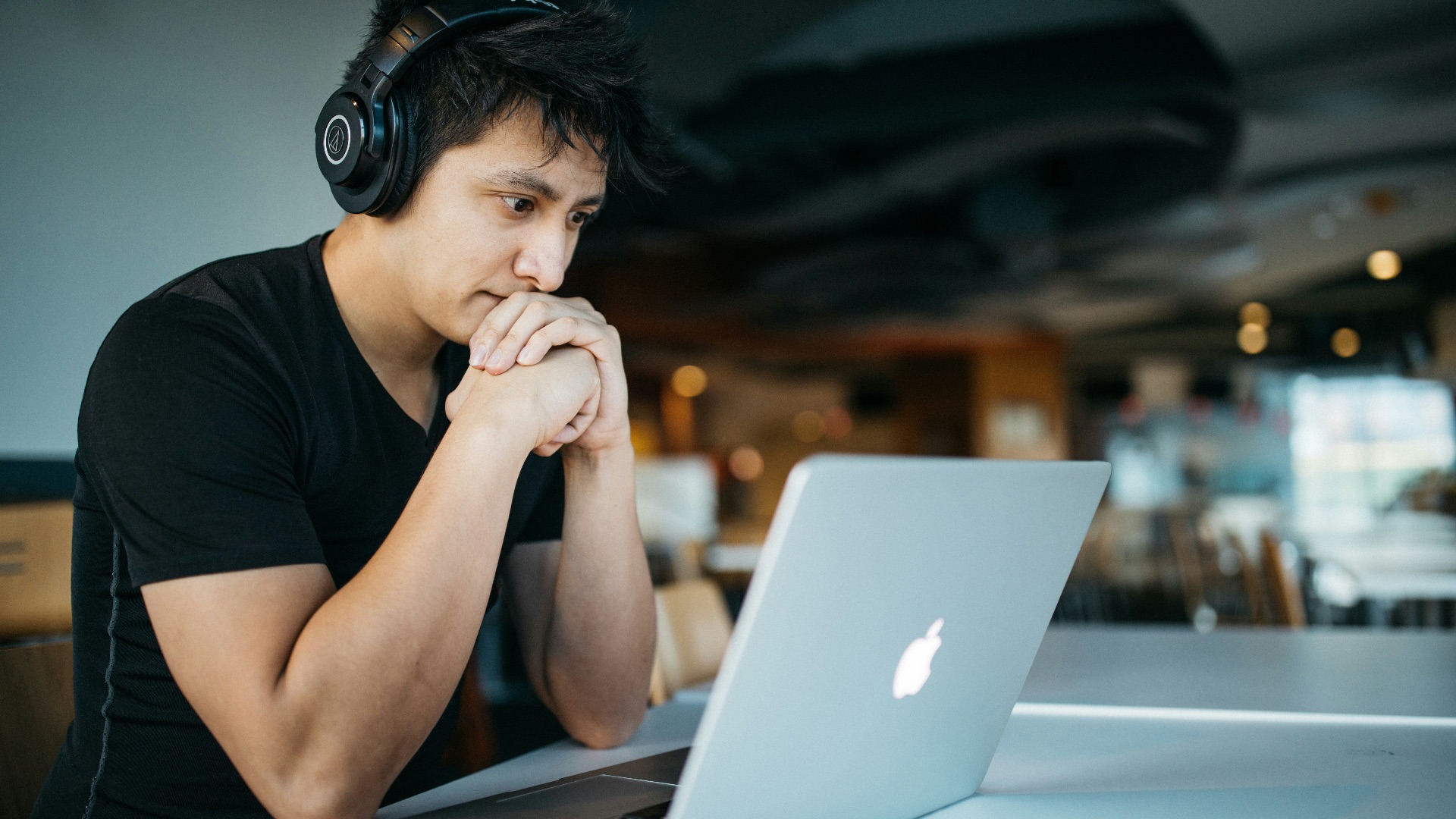 man wearing headphones while sitting on chair in front of MacBook