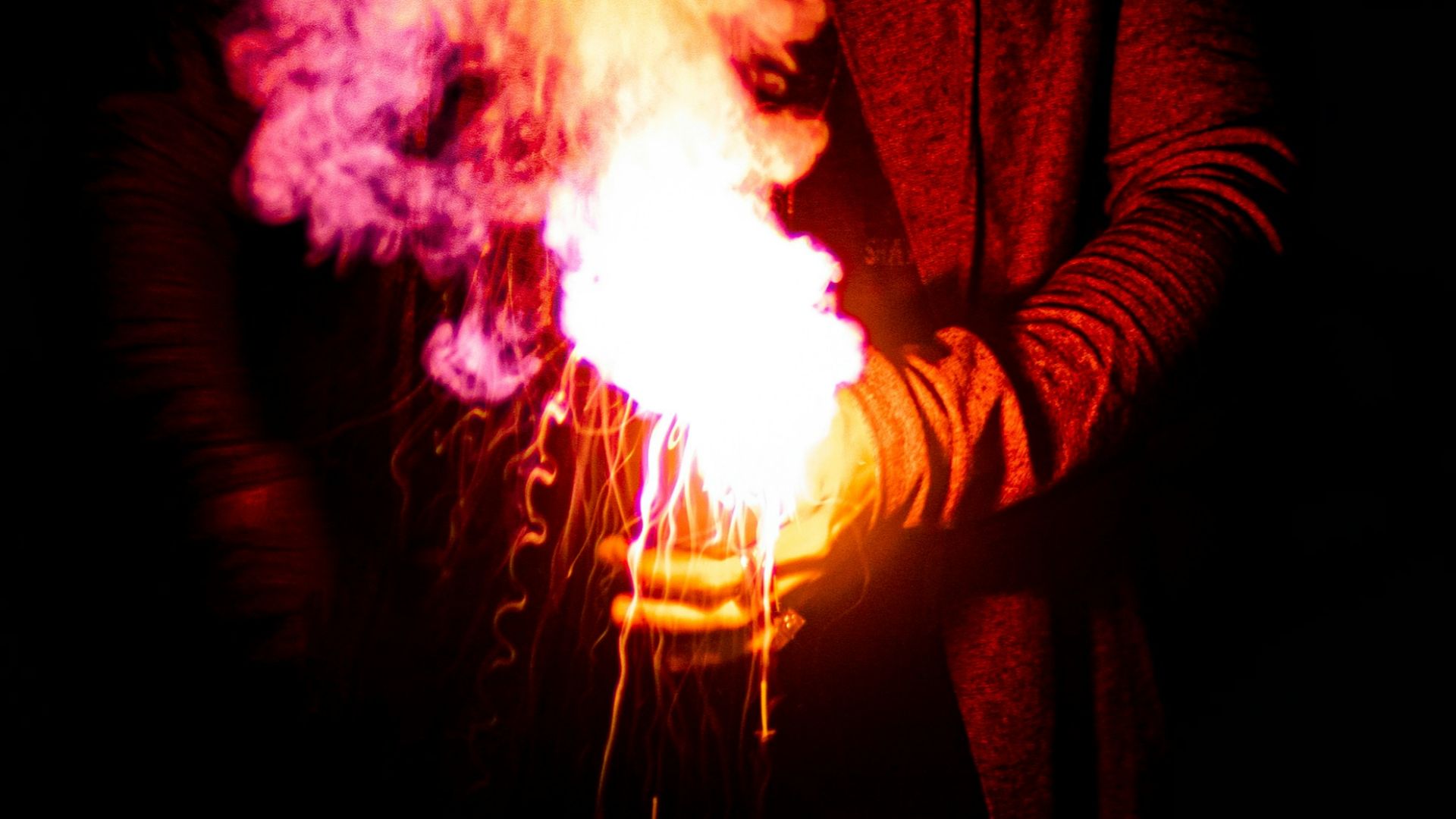 person in black mask holding purple and pink smoke