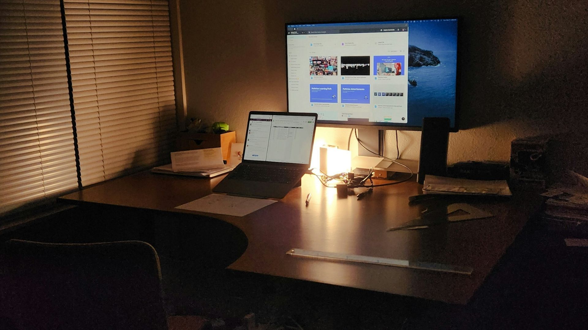 A dimly lit desk with a laptop and monitor.