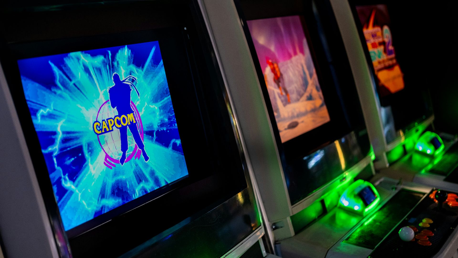 Row of glowing arcade game machines in darkness
