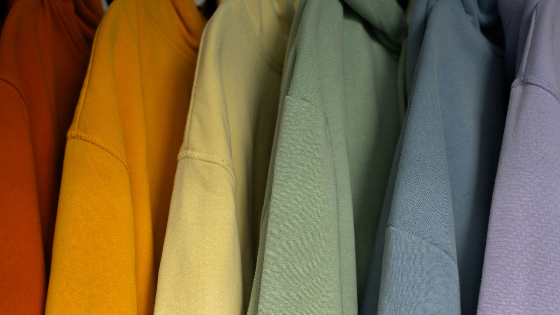 a row of different colored sweatshirts hanging on a rack