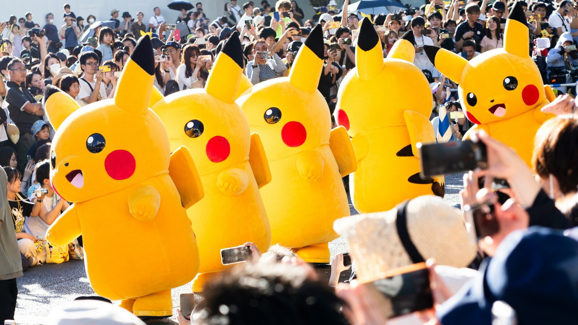 A large crowd of people with pokemon balloons in the shape of pikachu
