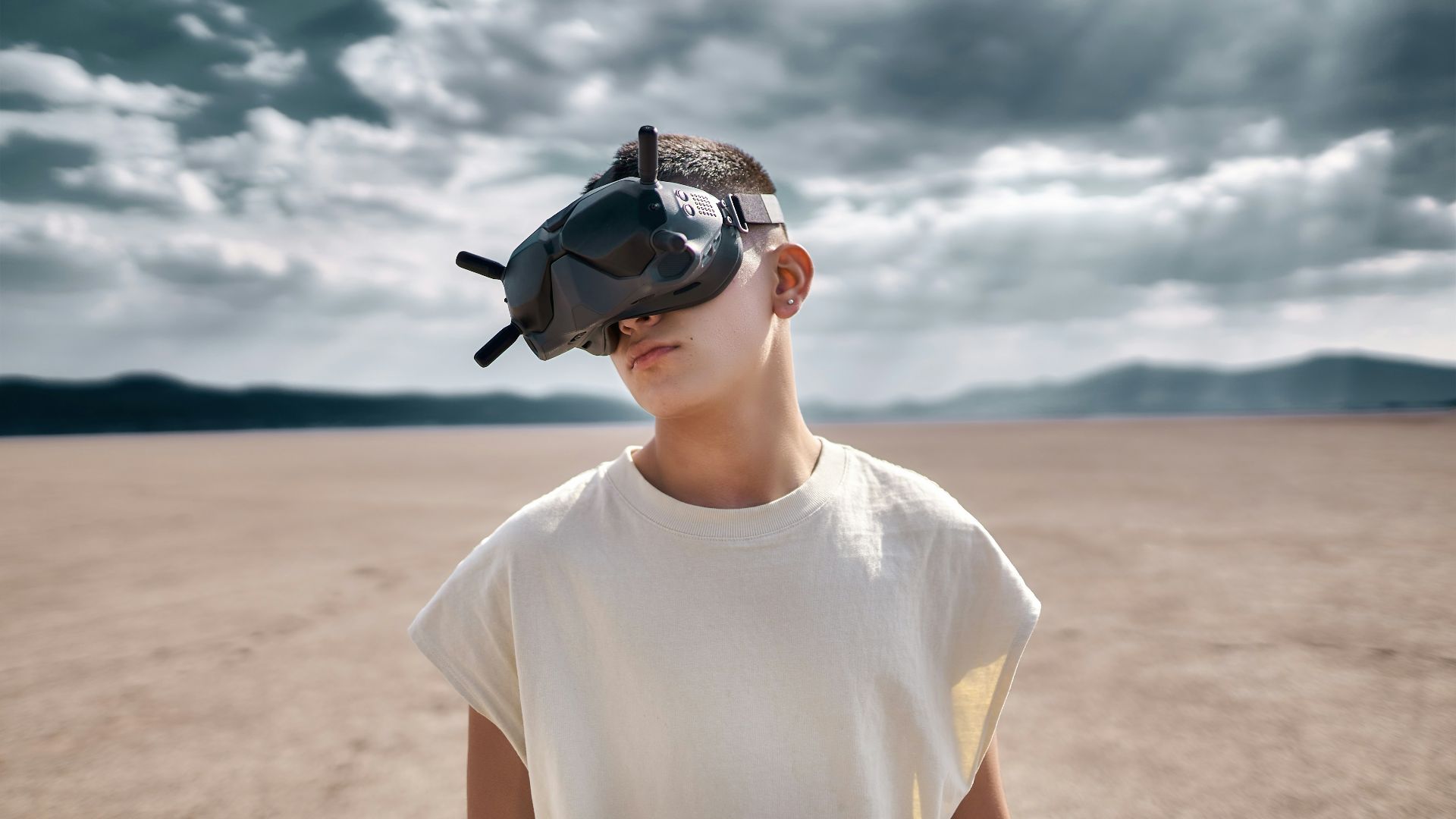 man in white crew neck t-shirt wearing black sunglasses standing on brown sand during daytime