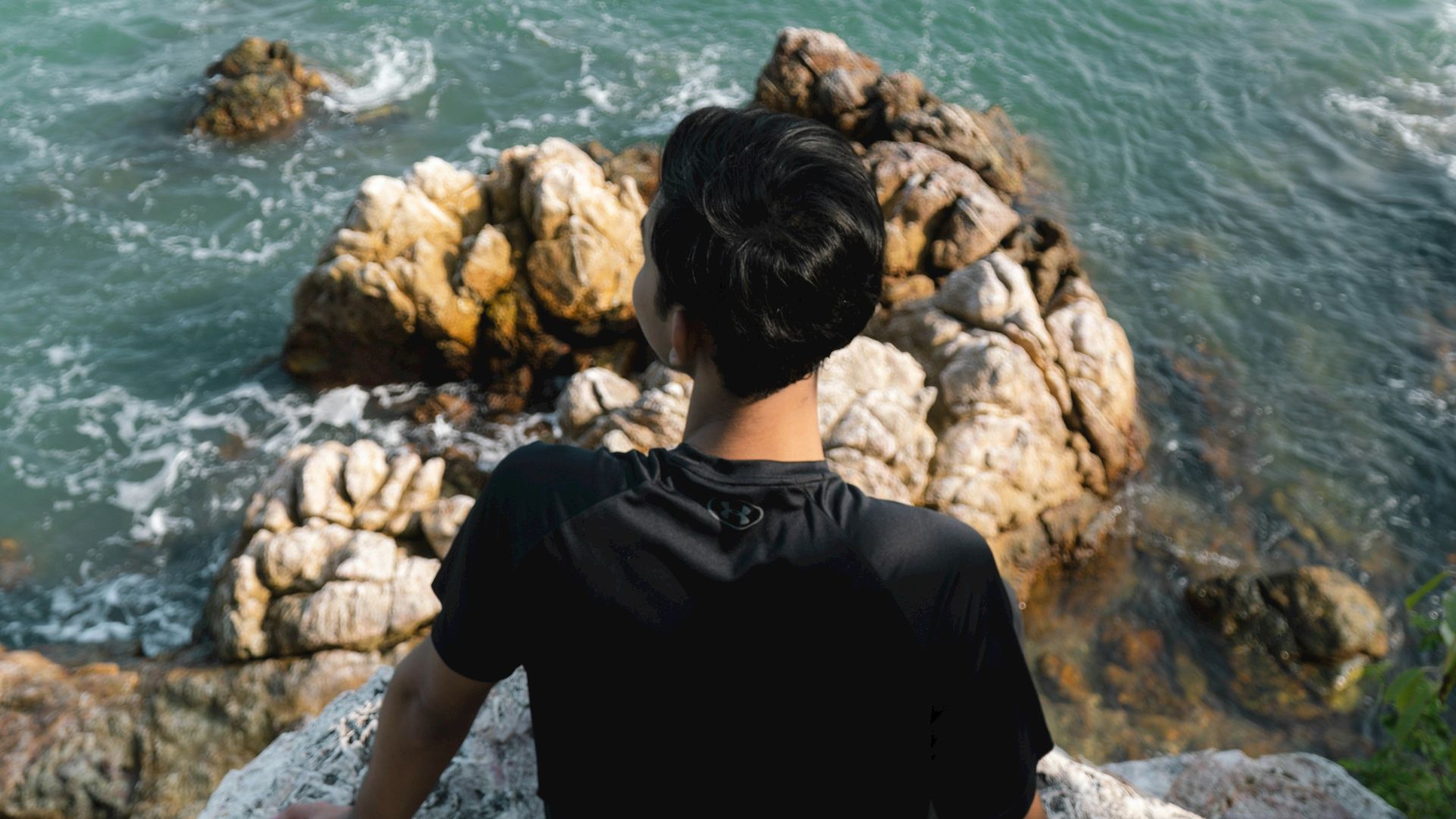 A man sitting on top of a rock next to the ocean