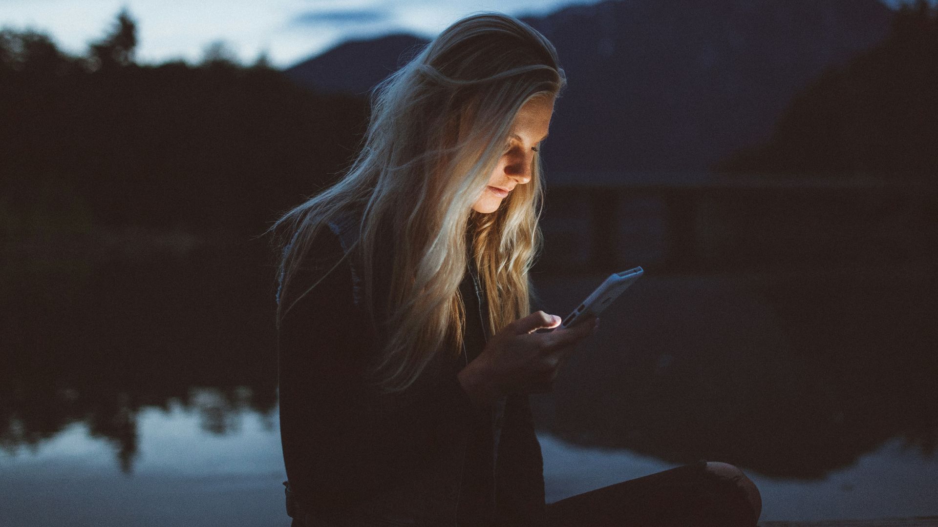 woman looking at phone beside body of water