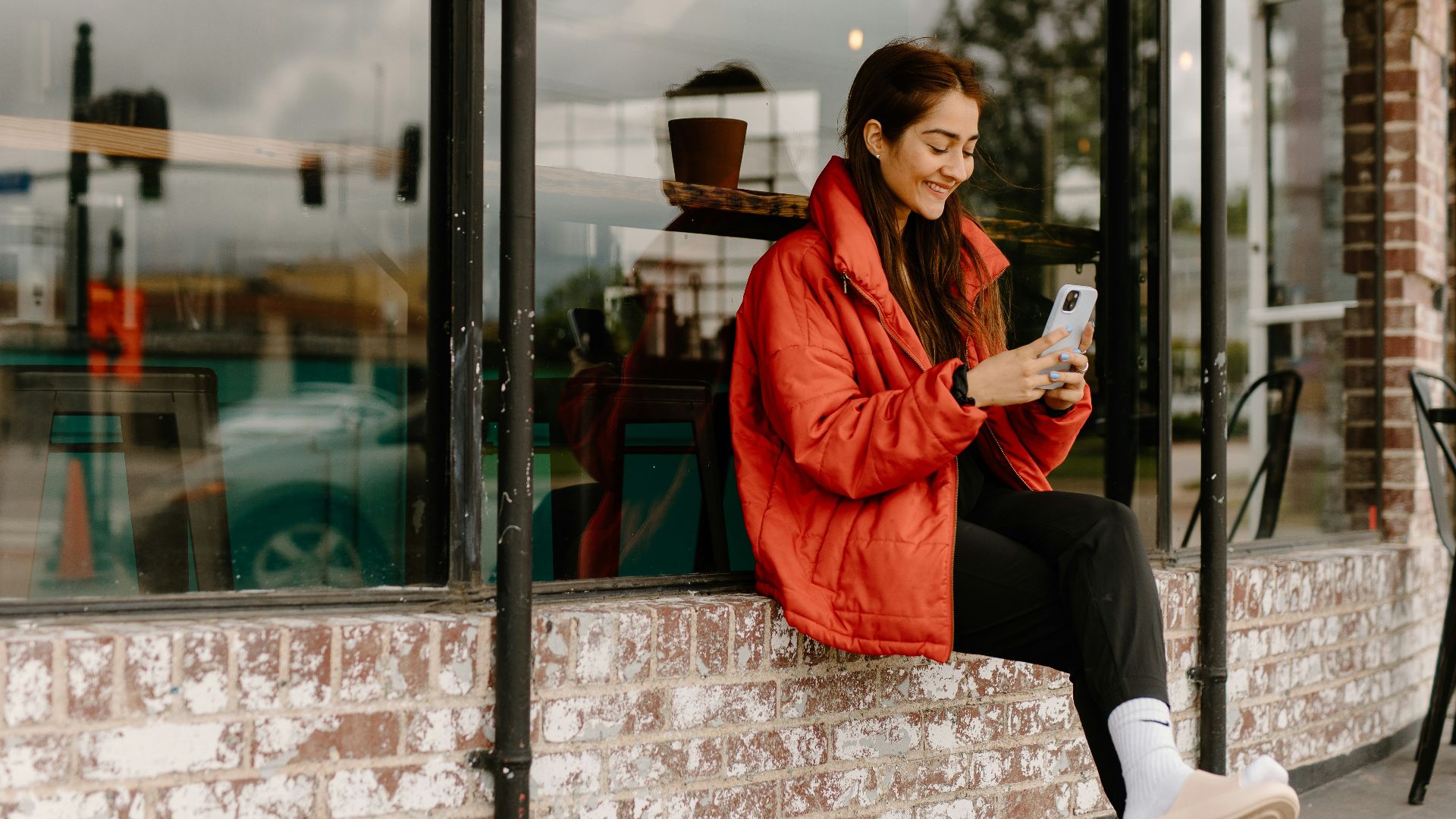 a woman sitting on a window sill looking at her cell phone