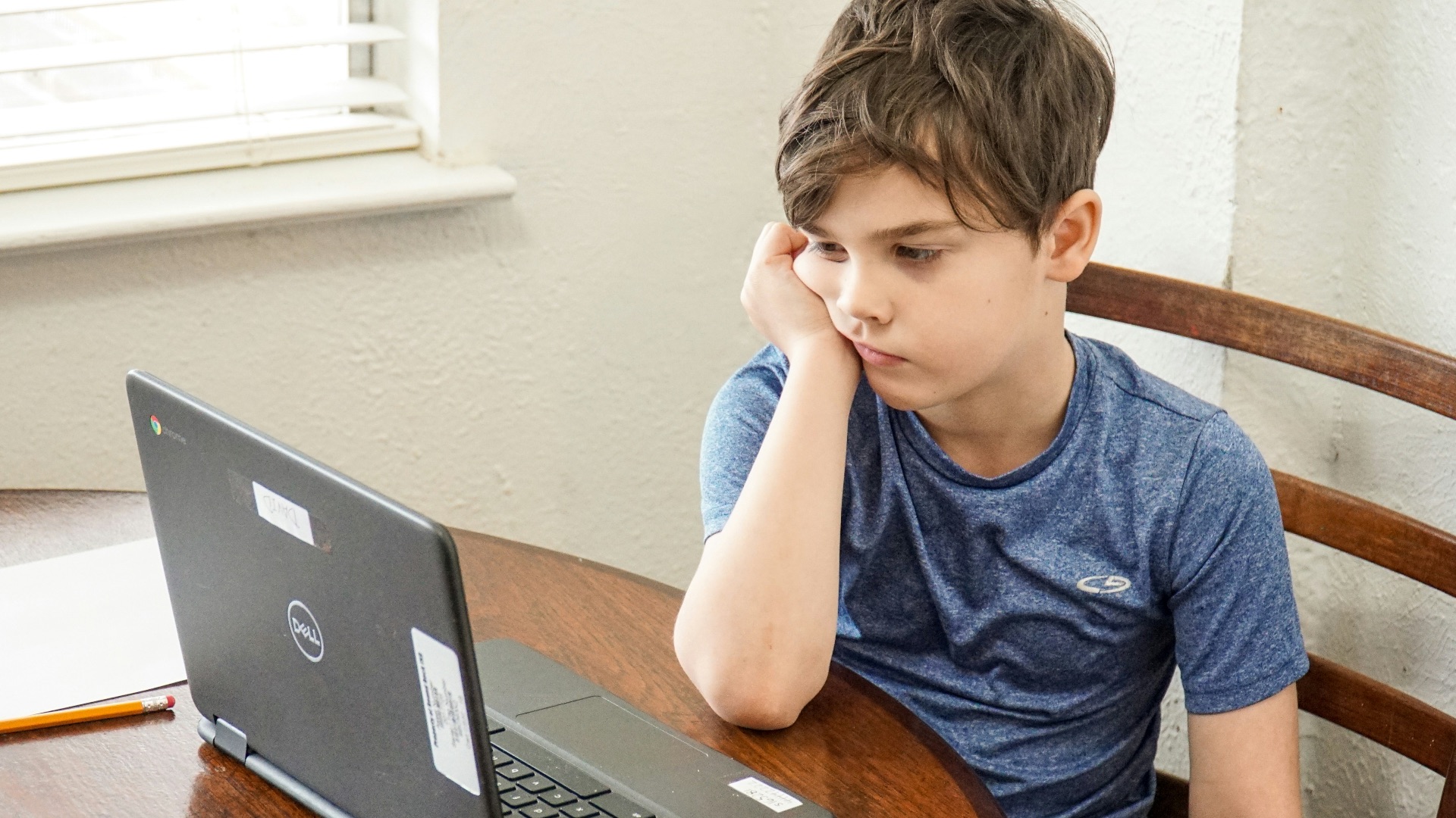 boy in blue crew neck t-shirt using macbook pro on brown wooden table