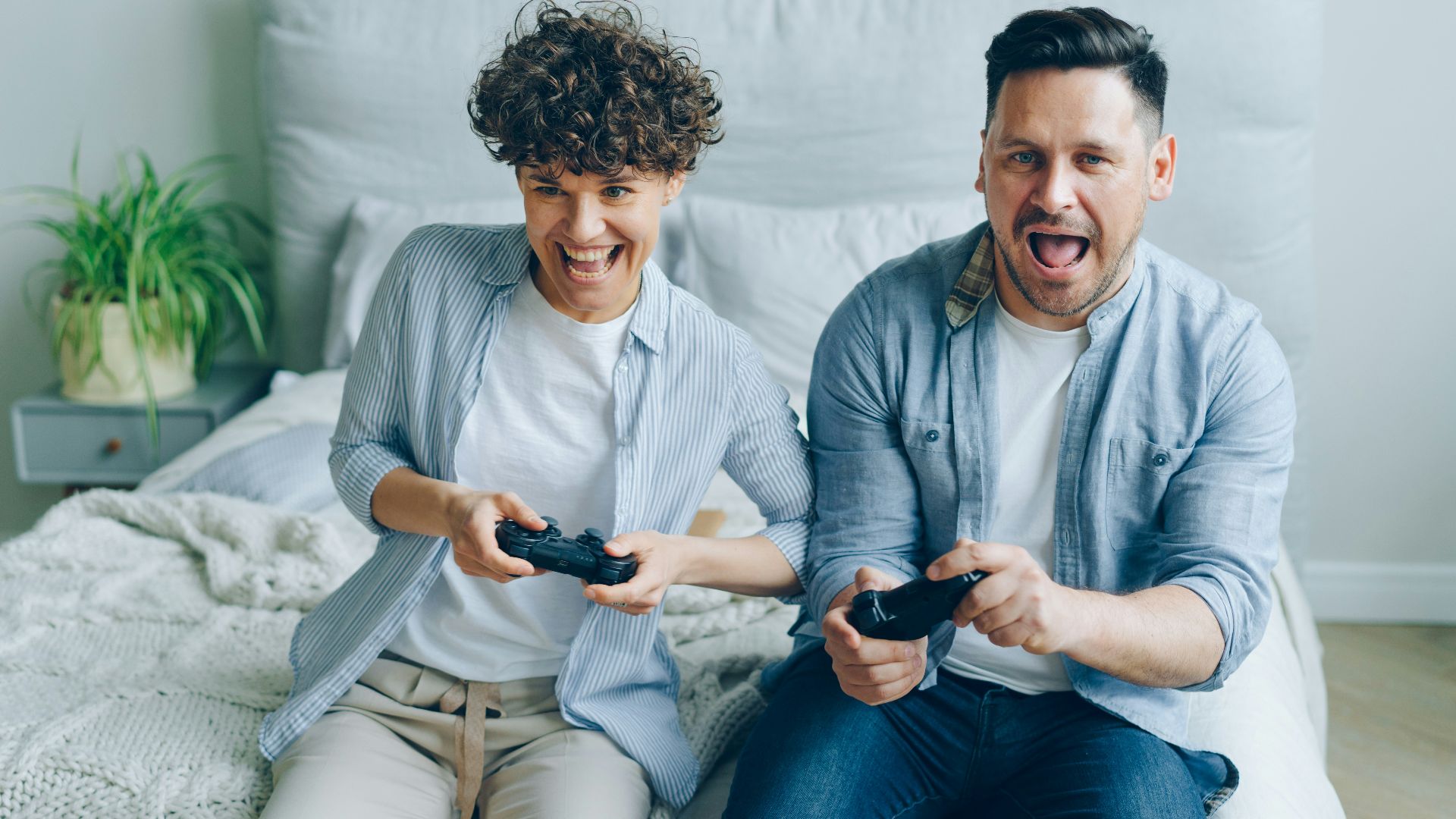 a man and a woman sitting on a bed playing a video game