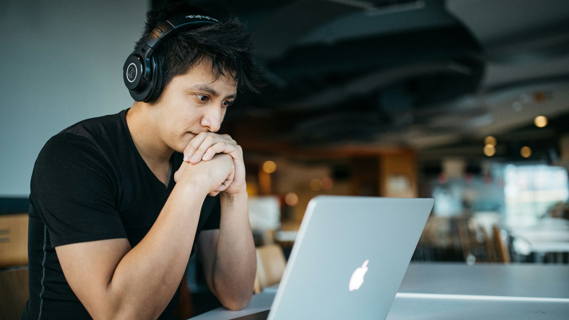 man wearing headphones while sitting on chair in front of MacBook