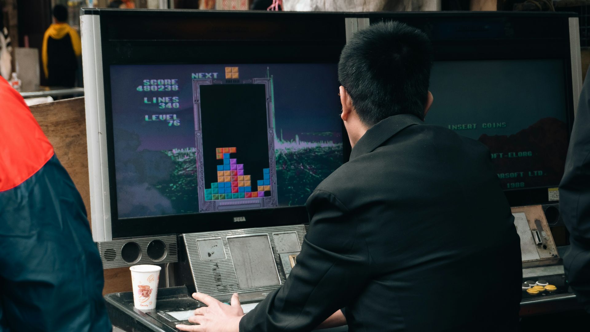 A man plays tetris on a vintage arcade game.