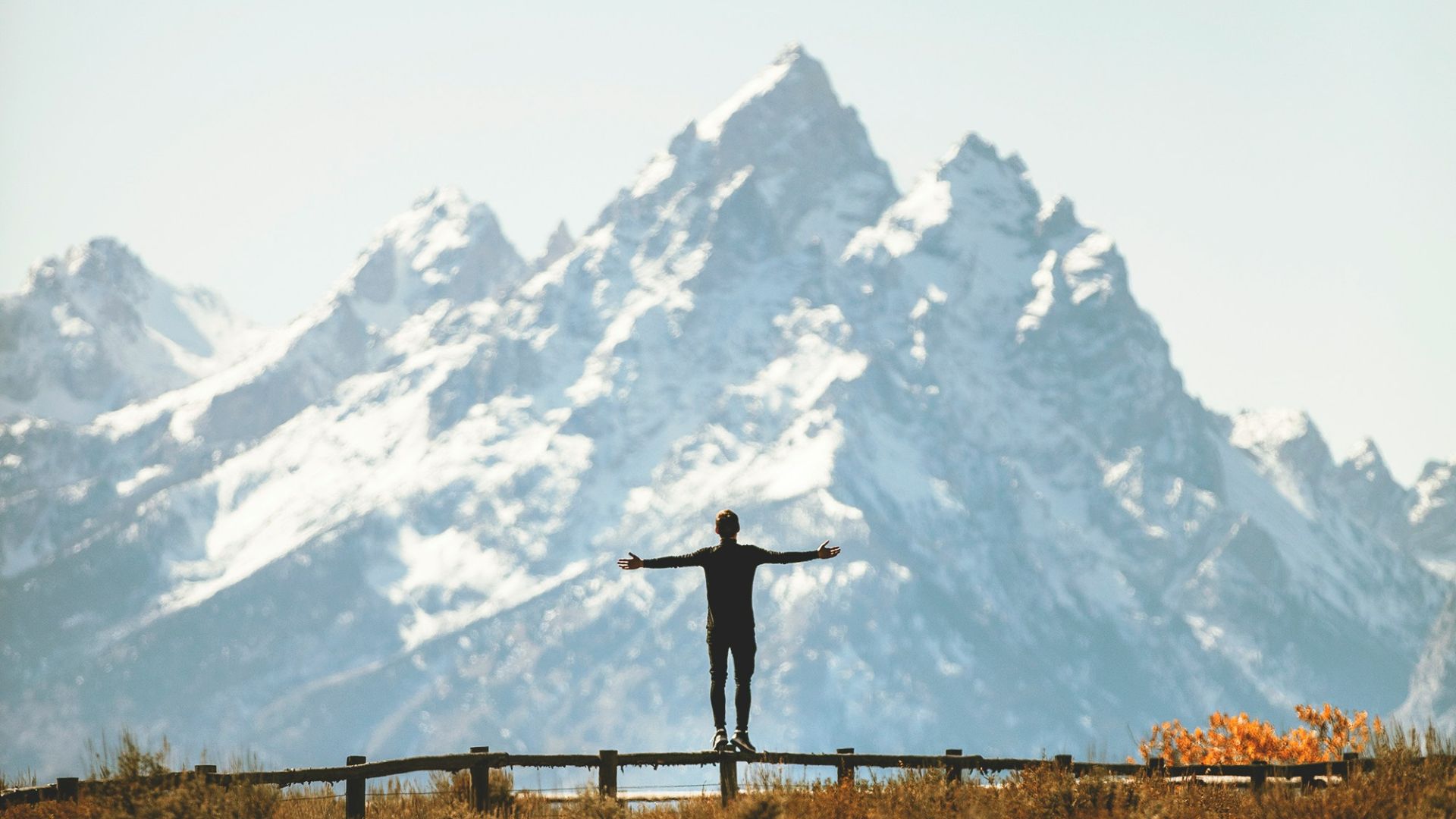 man standing on fence overlooking mountain range