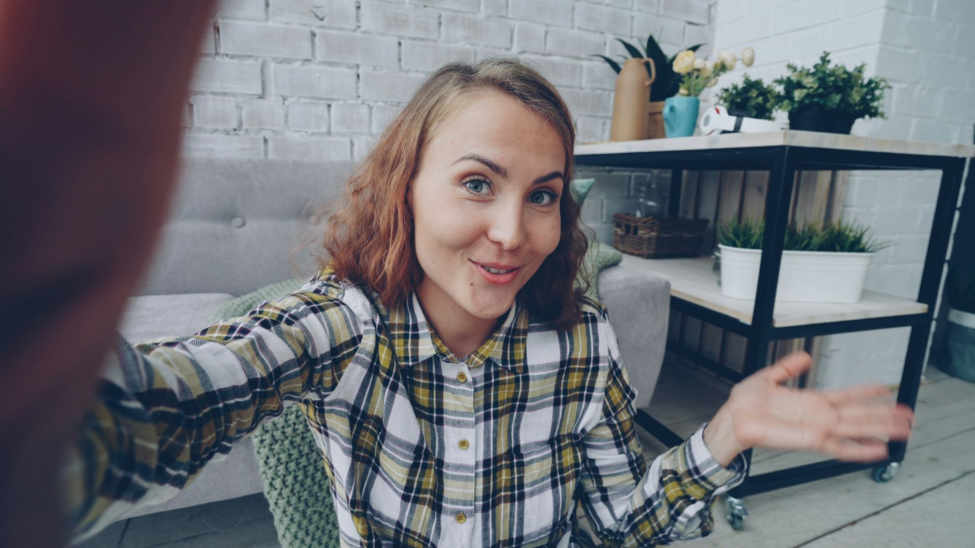 Young woman in plaid shirt filming herself at home.