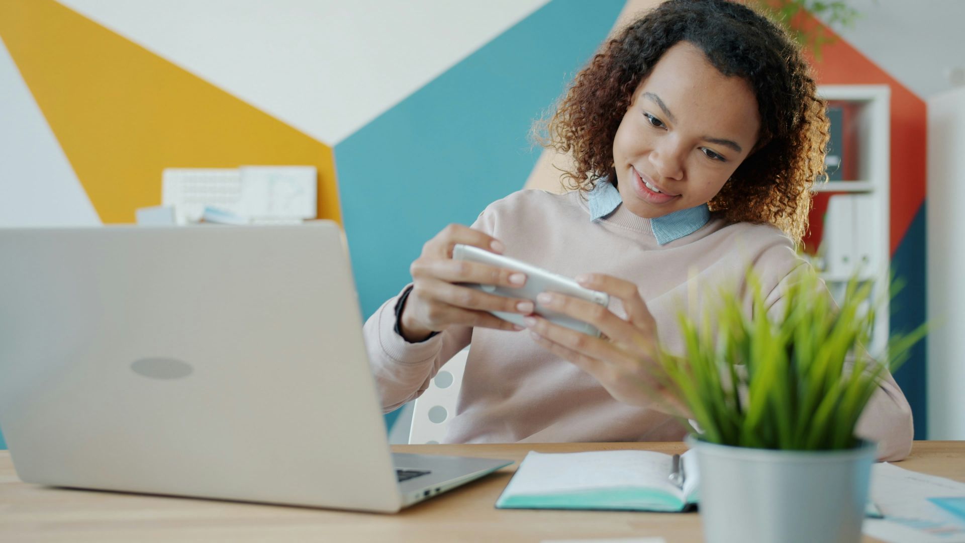Young woman playing game on smartphone at desk