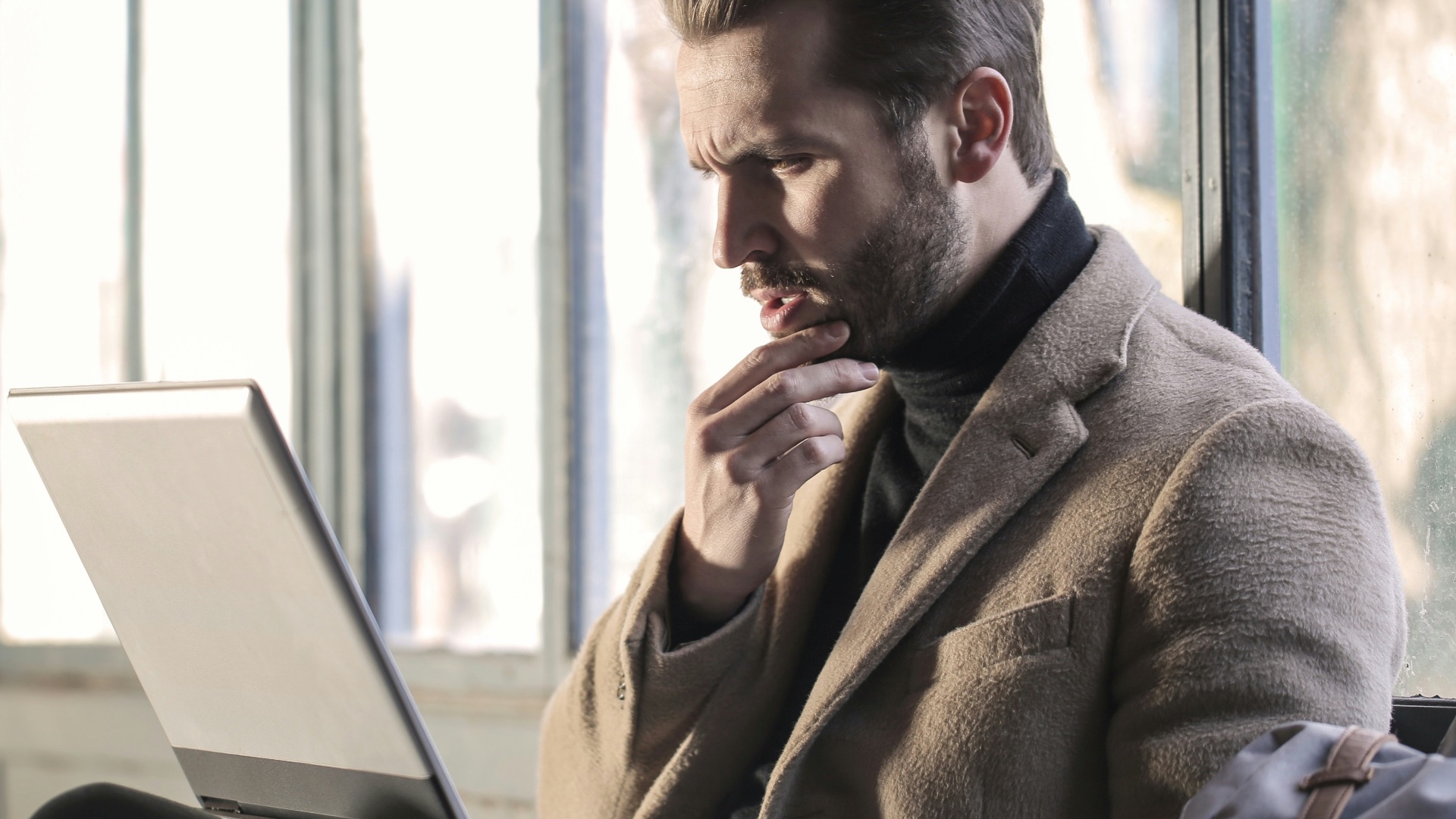 man holding his chin facing laptop computer