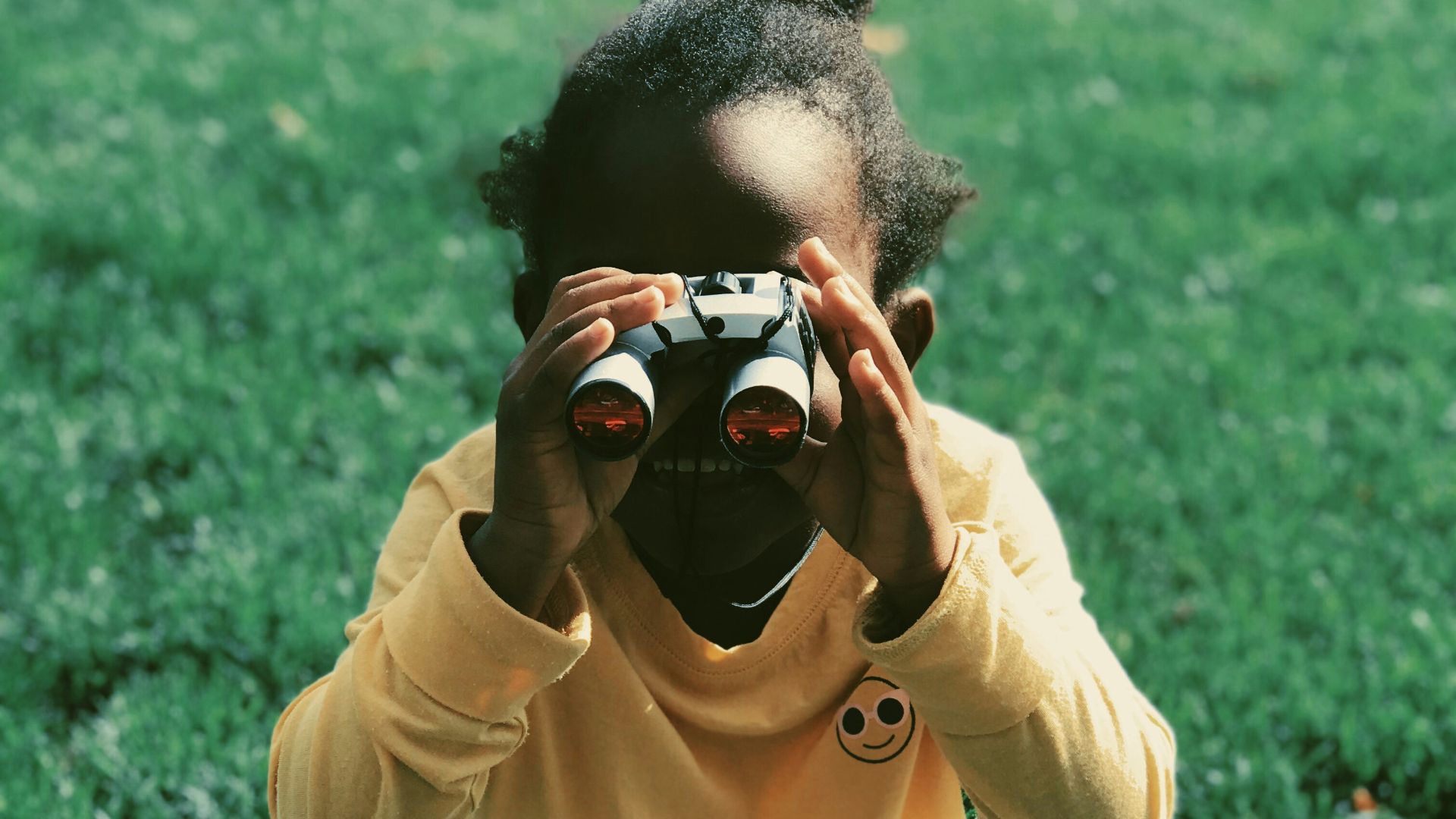 girl sitting on grass field holding binoculars