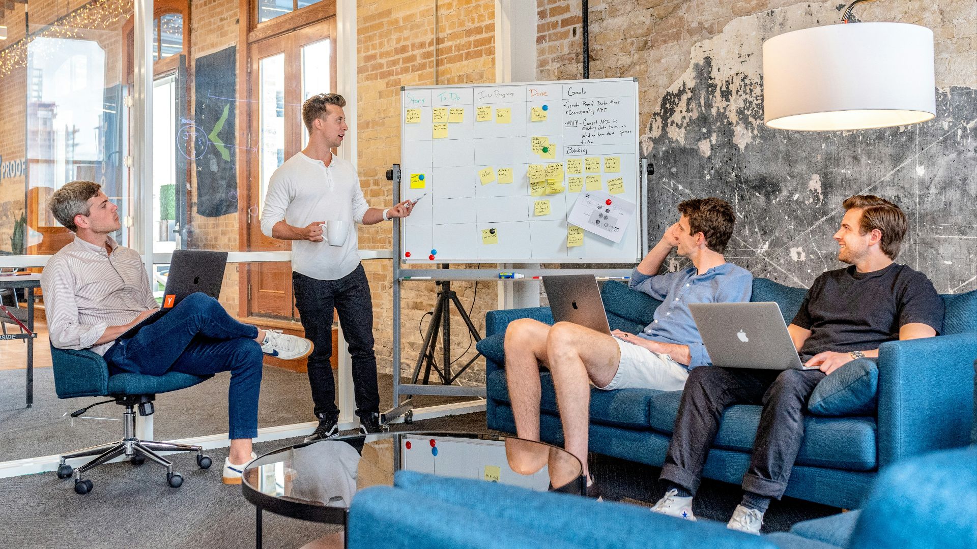 three men sitting while using laptops and watching man beside whiteboard