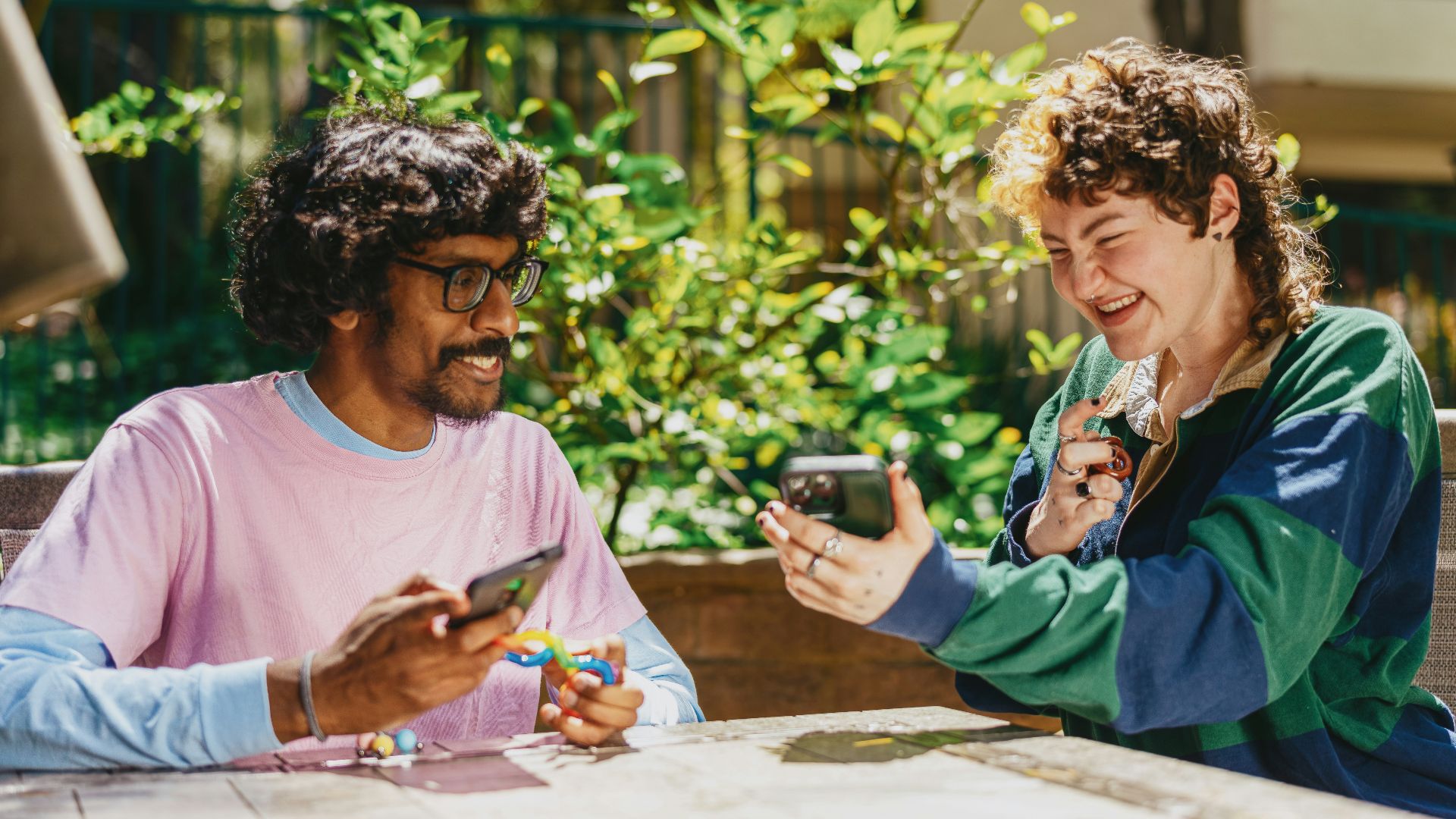 Two autistic friends sitting outside using stim toys and laughing at their phones