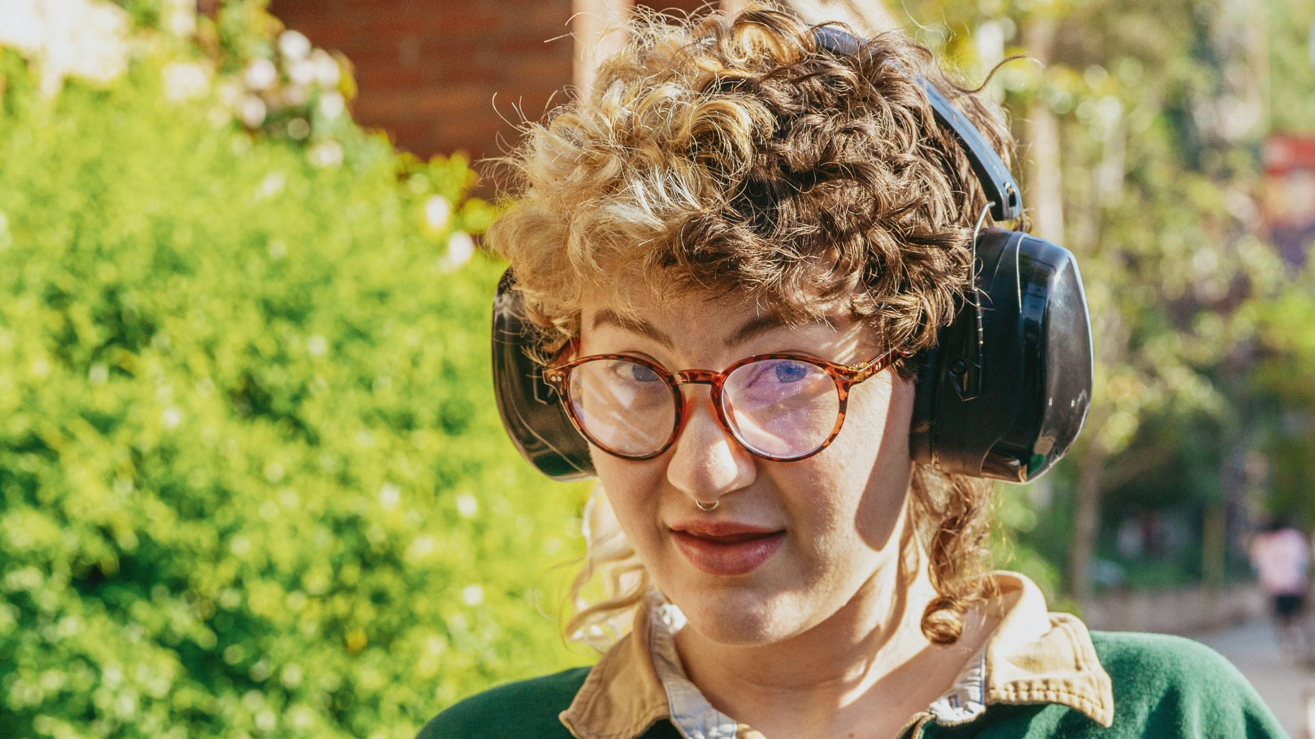 Portrait of a nonbinary autistic person outdoors using headphones