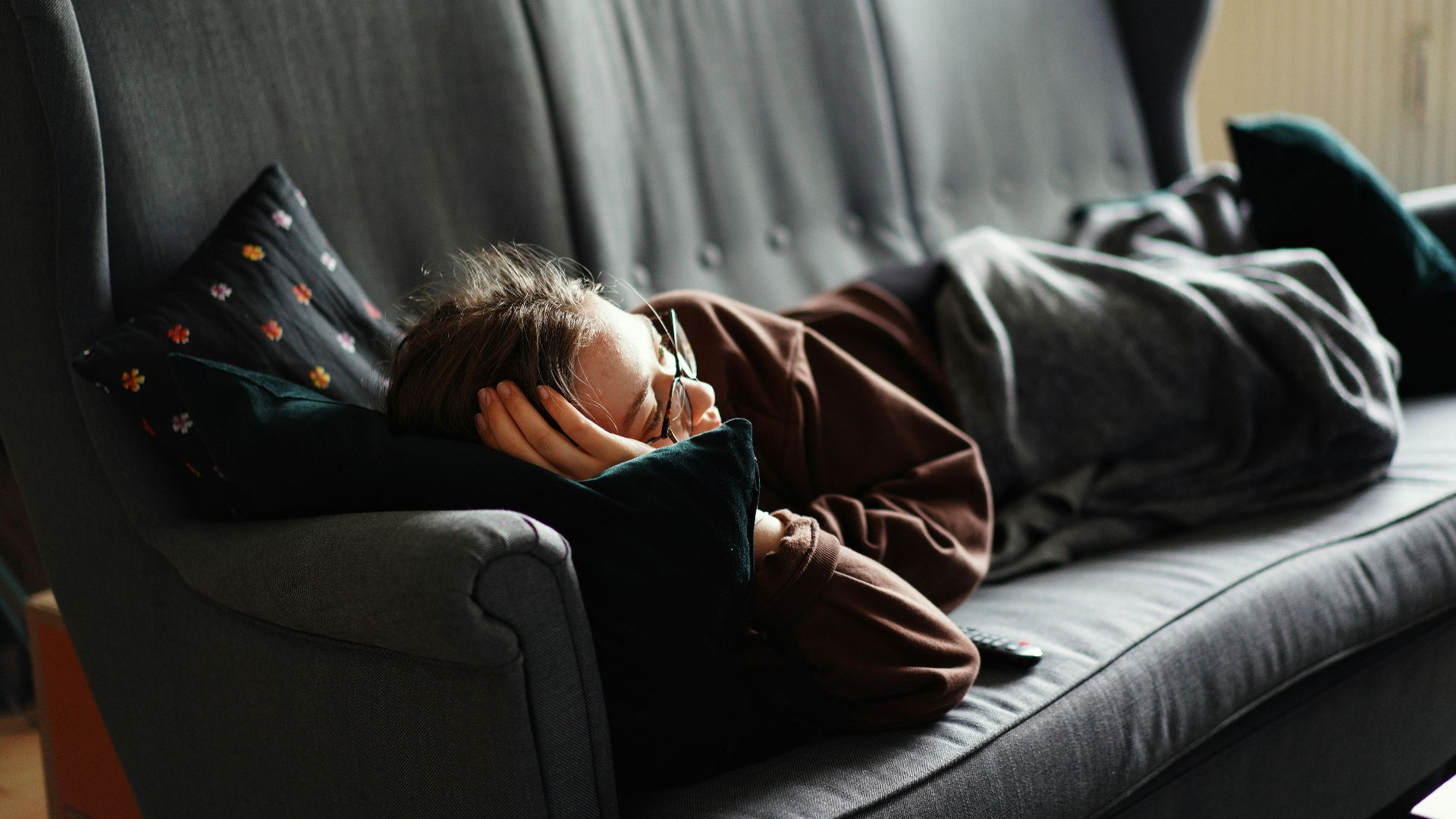 woman in pink jacket lying on gray couch