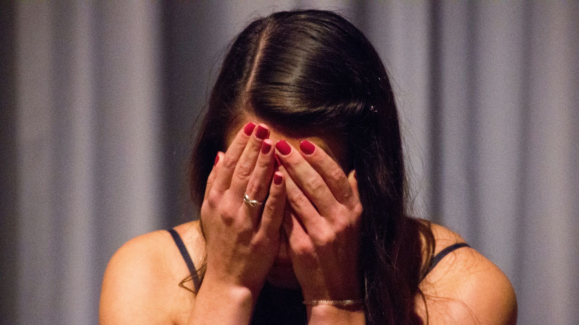 woman in black tank top covering her face with her hands