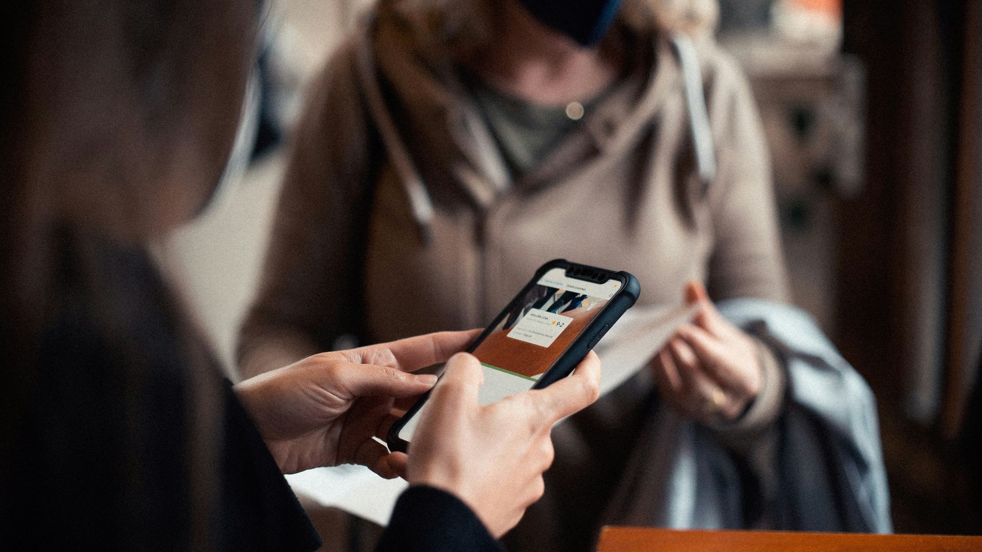 woman in brown coat holding black smartphone