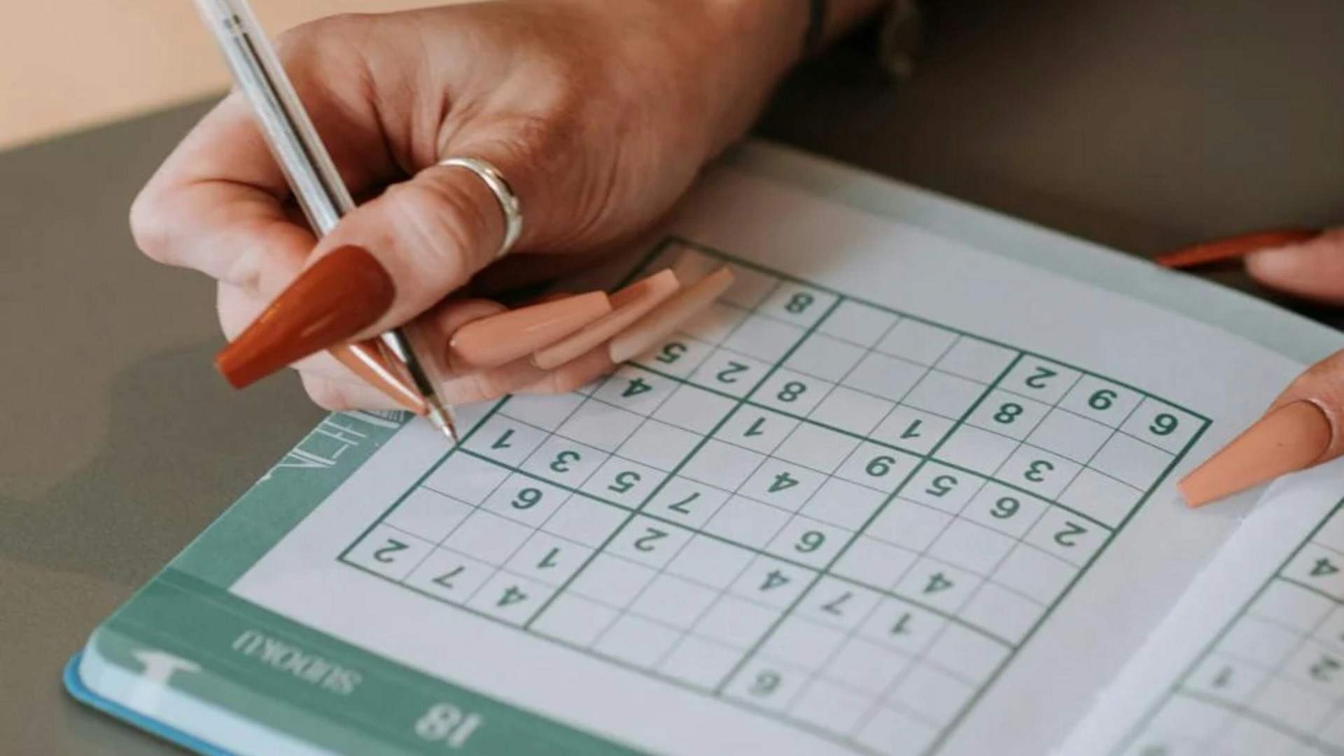 A woman is writing on a crossword puzzle book