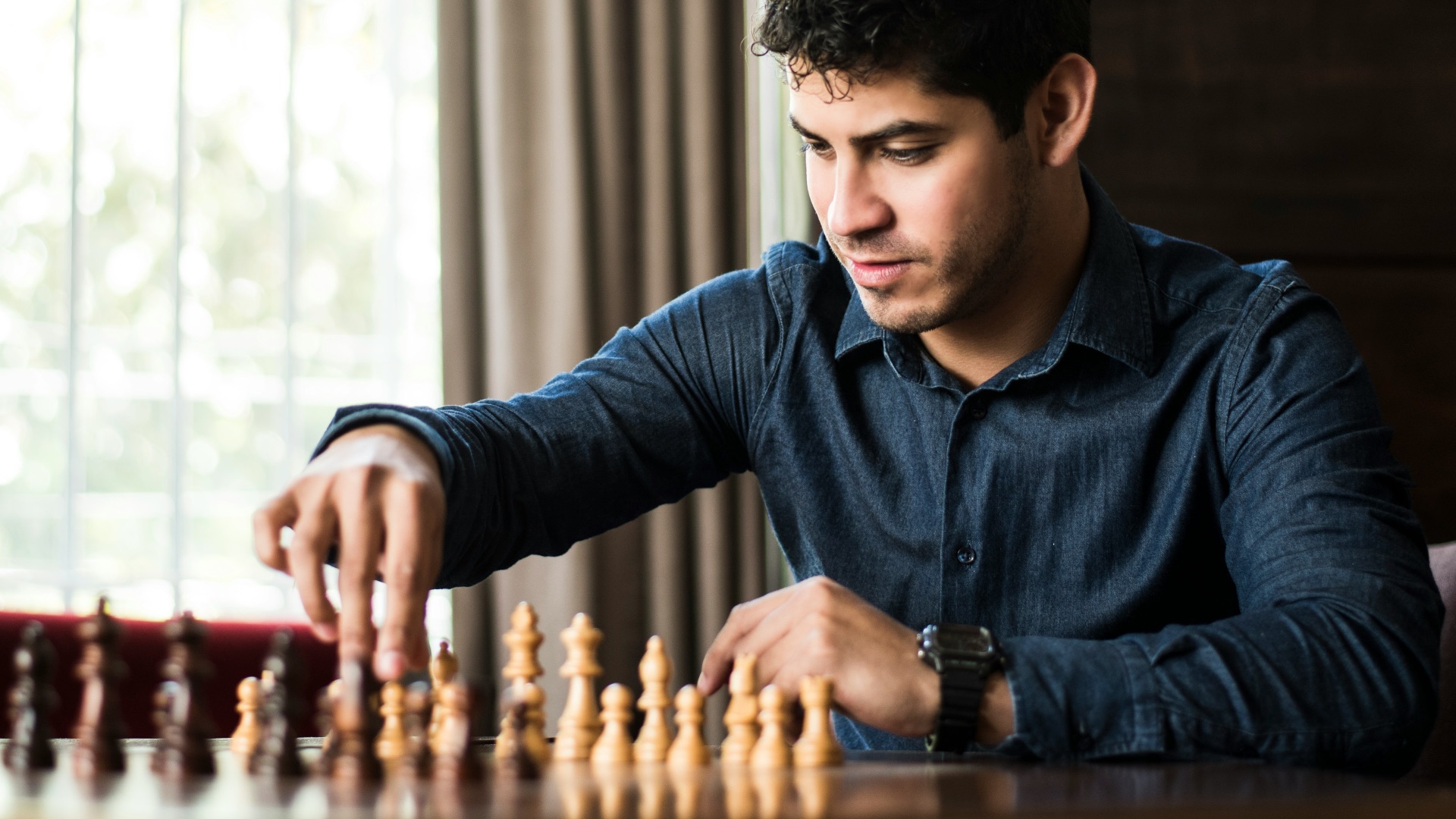 man in blue dress shirt sitting down and playing chess game