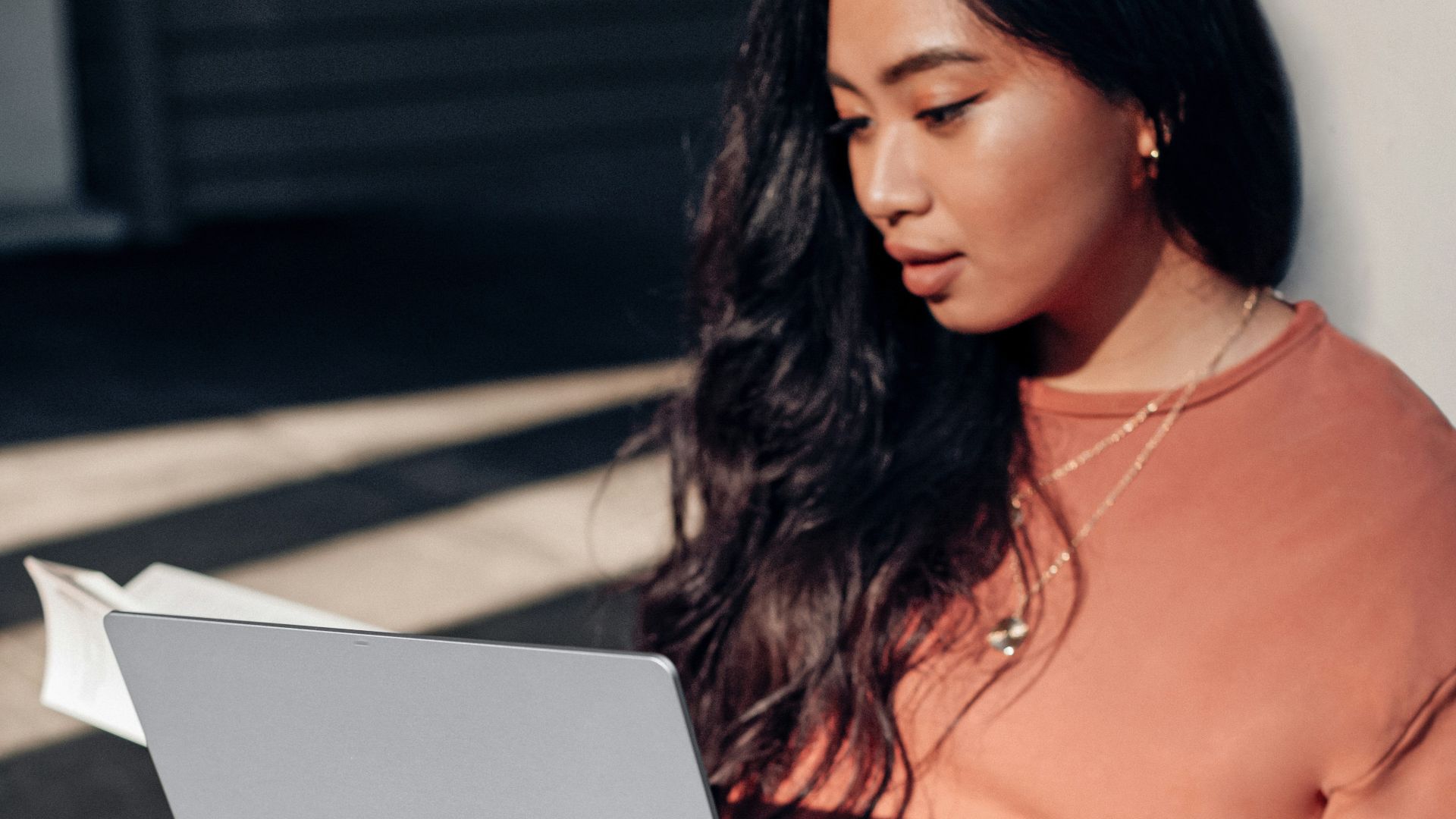 woman in orange long sleeve shirt and white pants sitting on floor using Surface Laptop