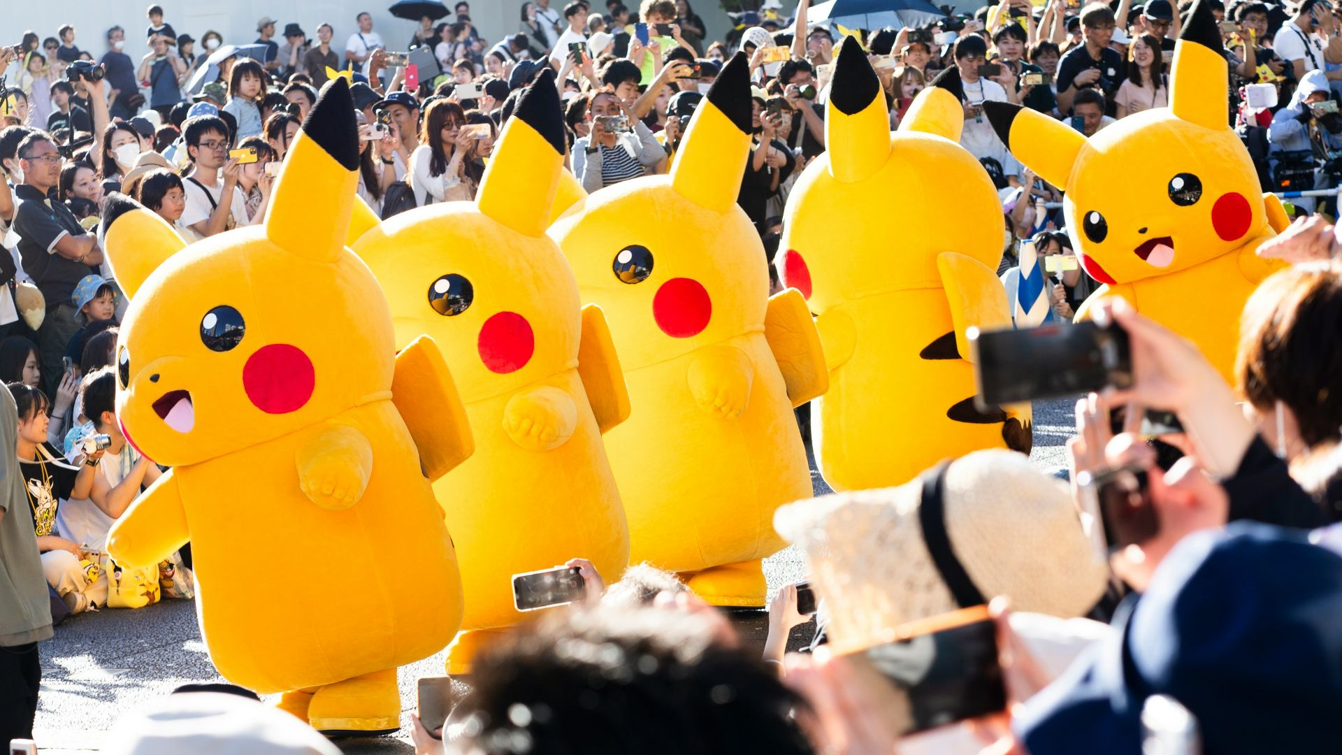 A large crowd of people with pokemon balloons in the shape of pikachu