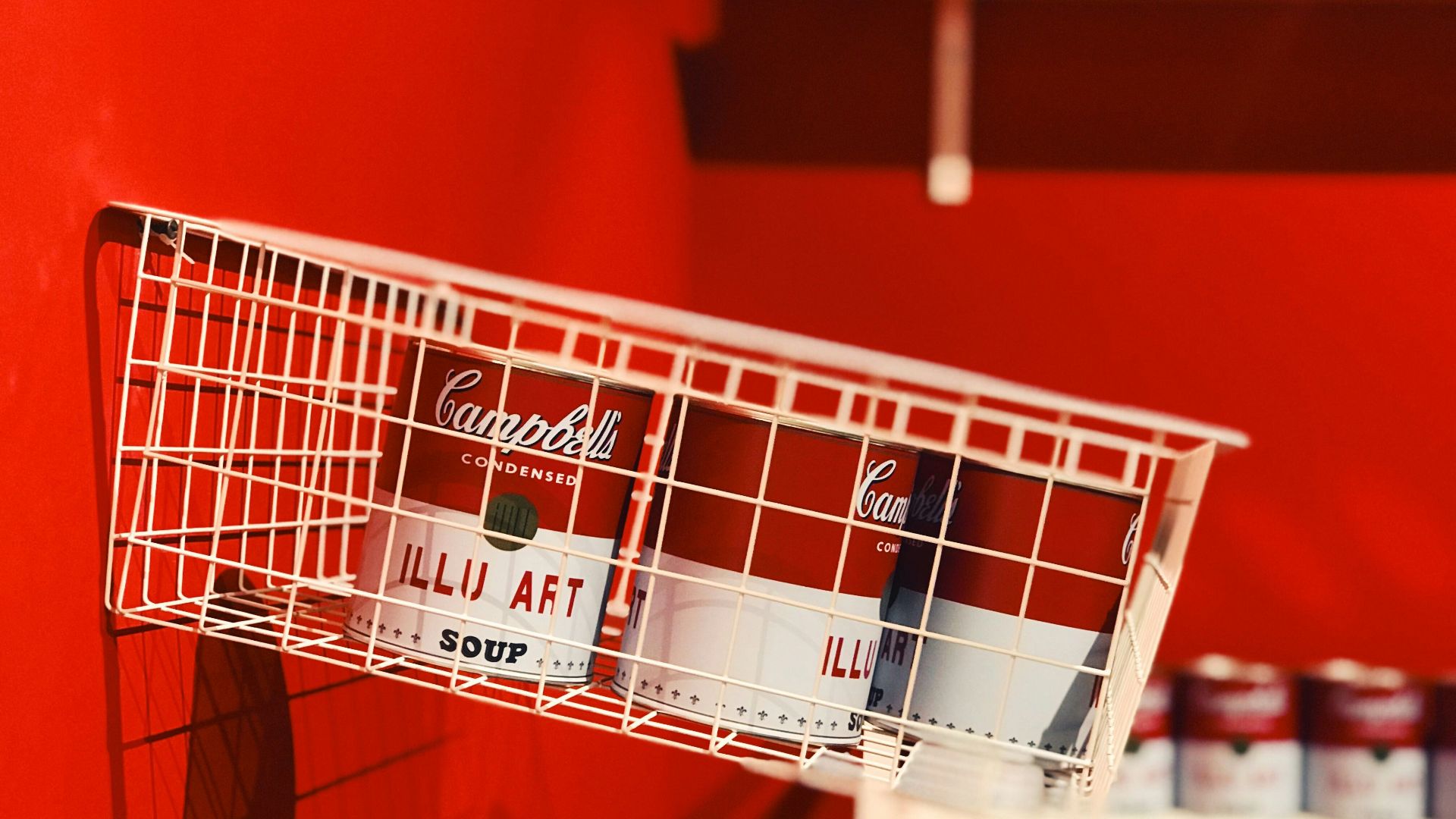 a red wall with a white wire basket holding cans of coca - cola