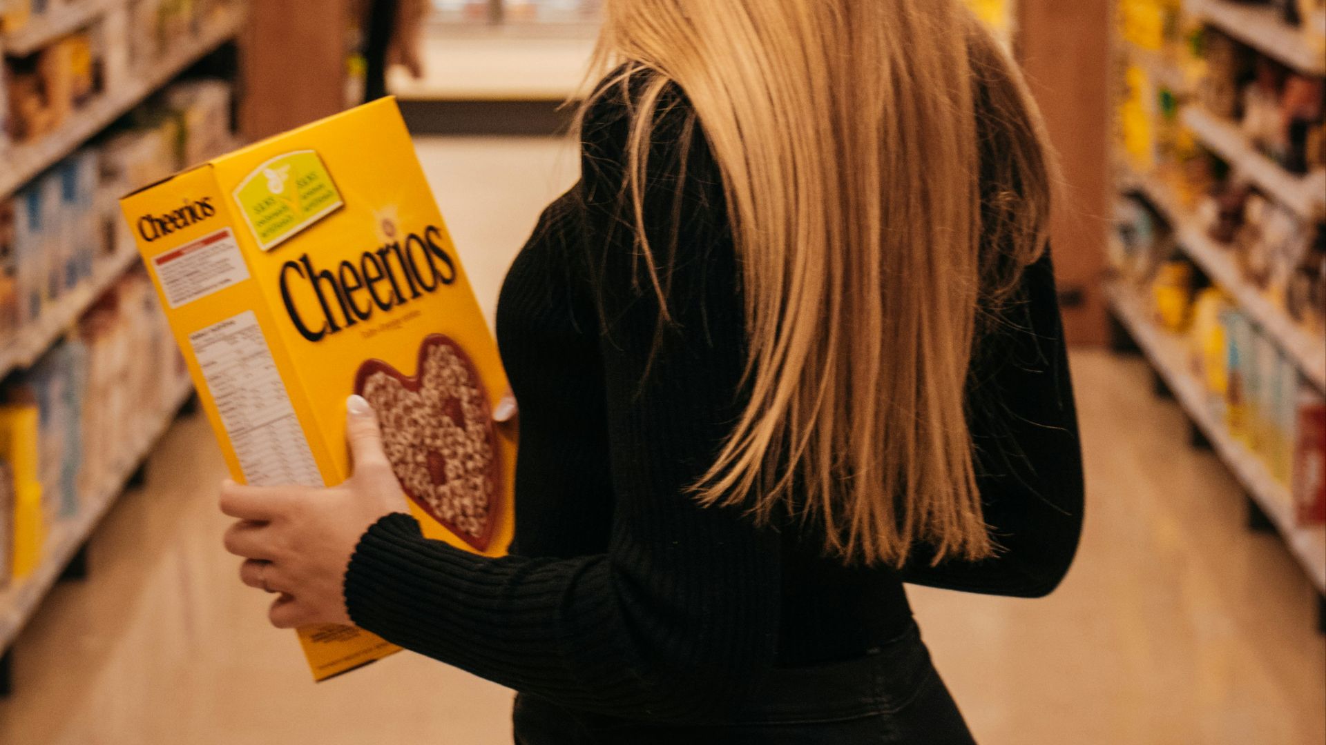 woman wearing black long-sleeved shirt holding Cheerios cereal box standing