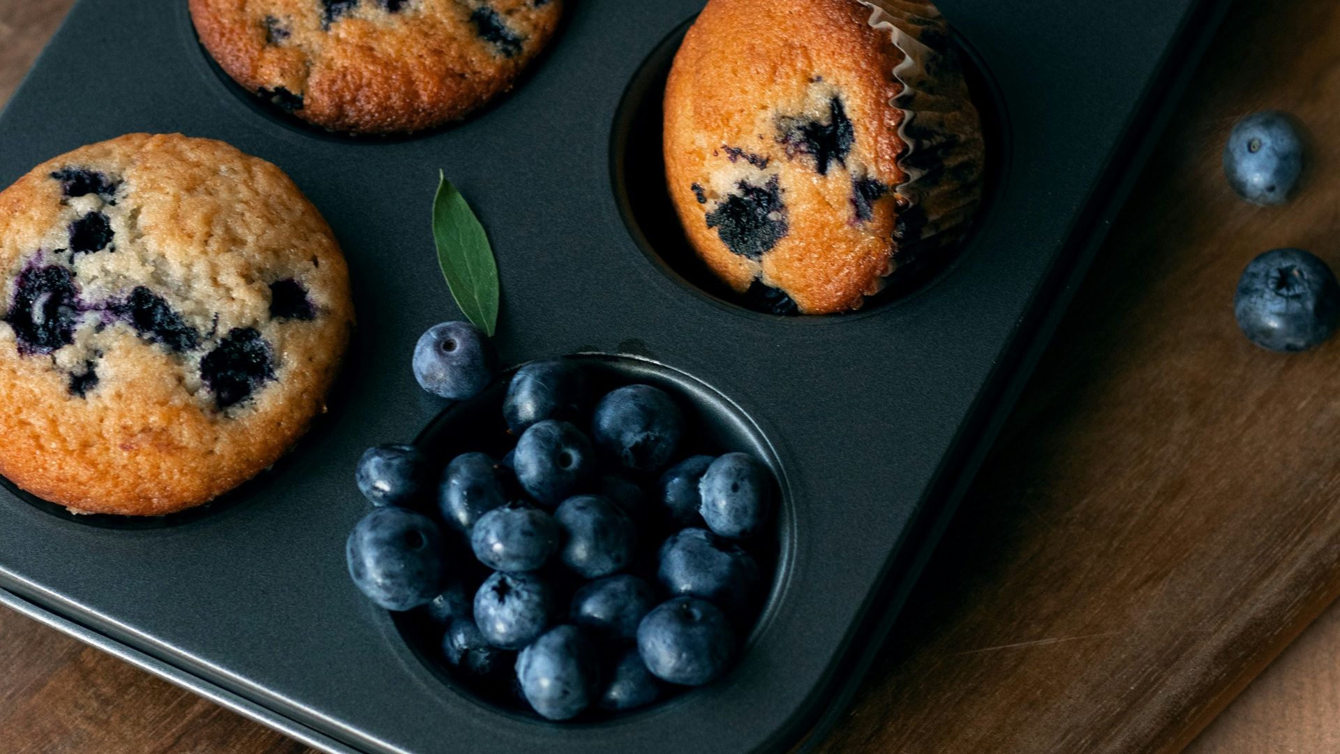 Blueberry muffins in a muffin tin on a cutting board