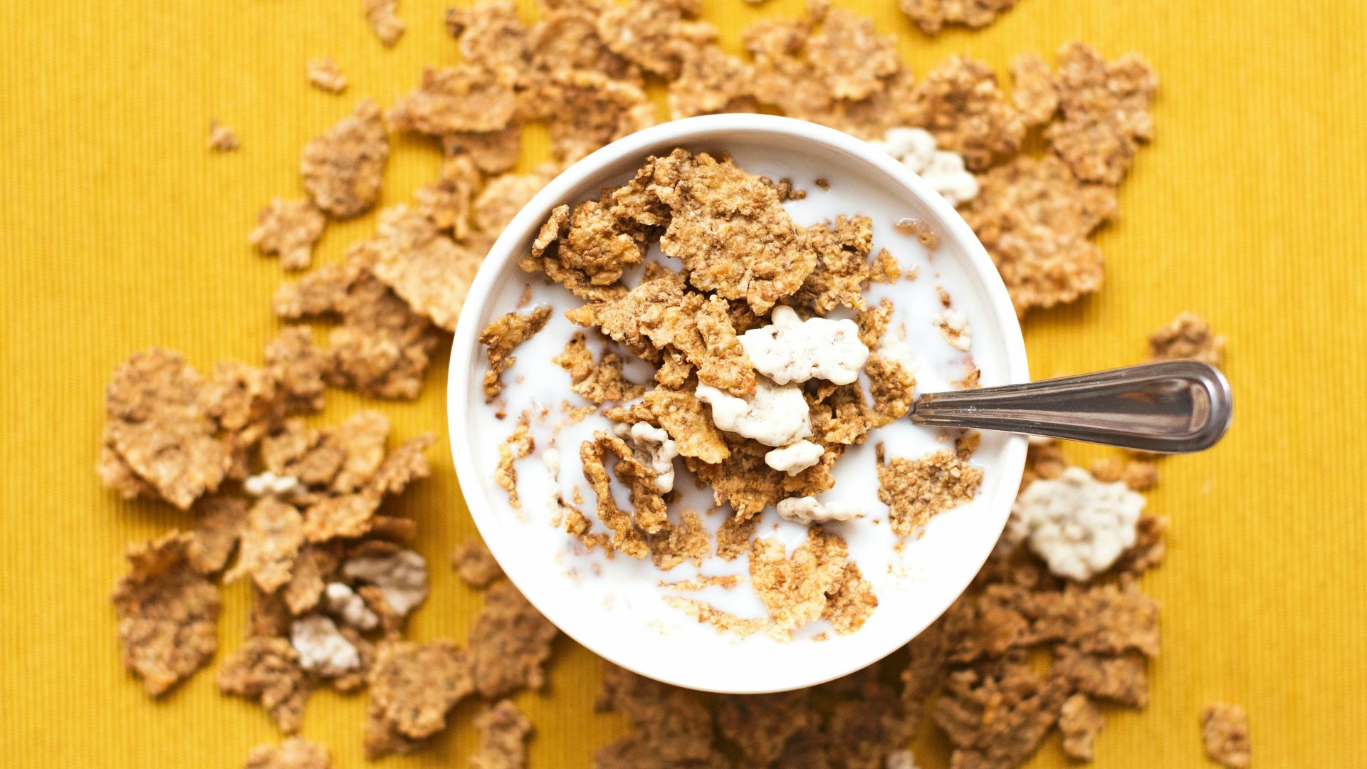 top view of corn flakes in bowl with milk and silver spoon