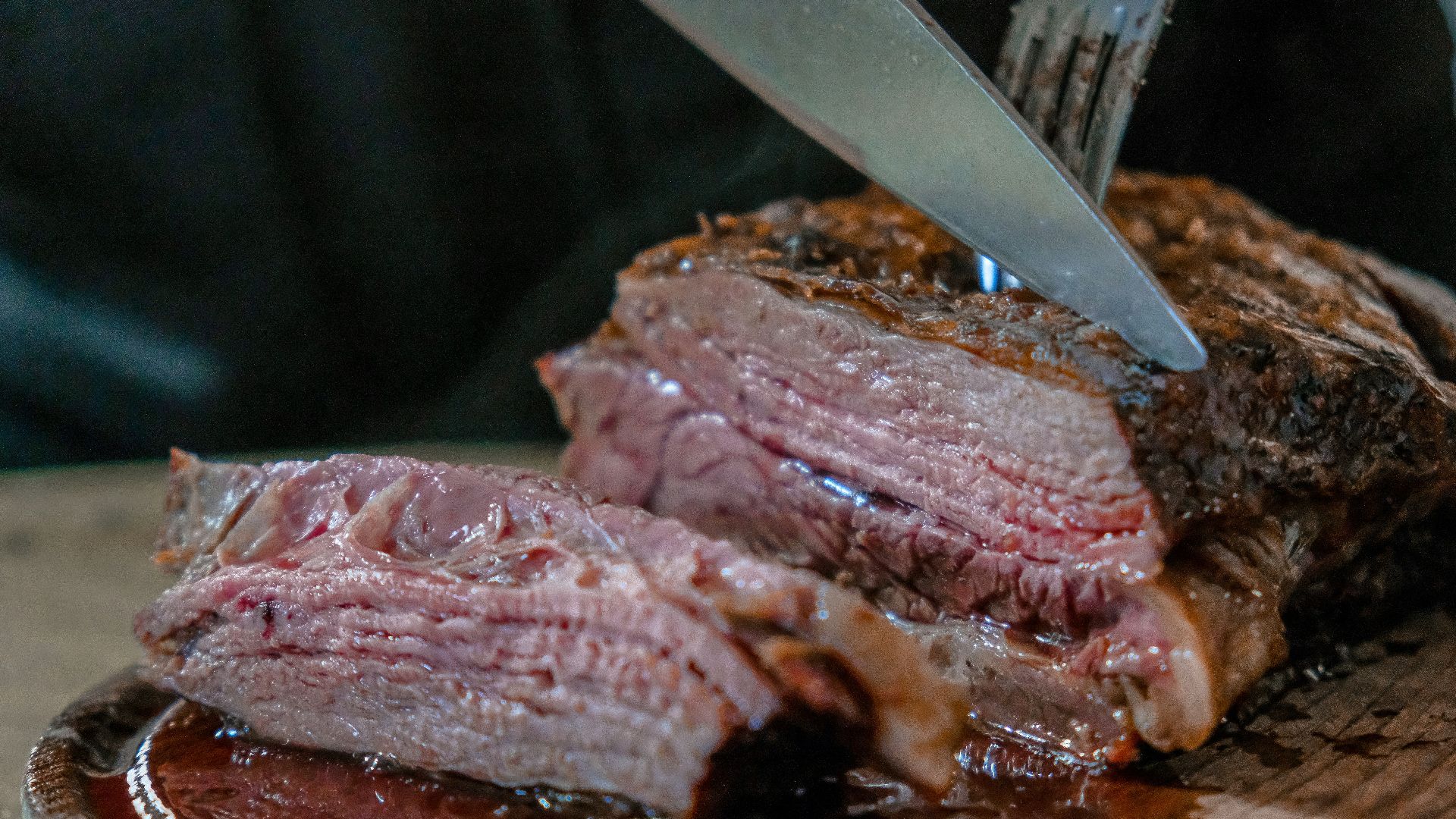 person slicing juicy medium rare meat on top of brown wooden cutting board