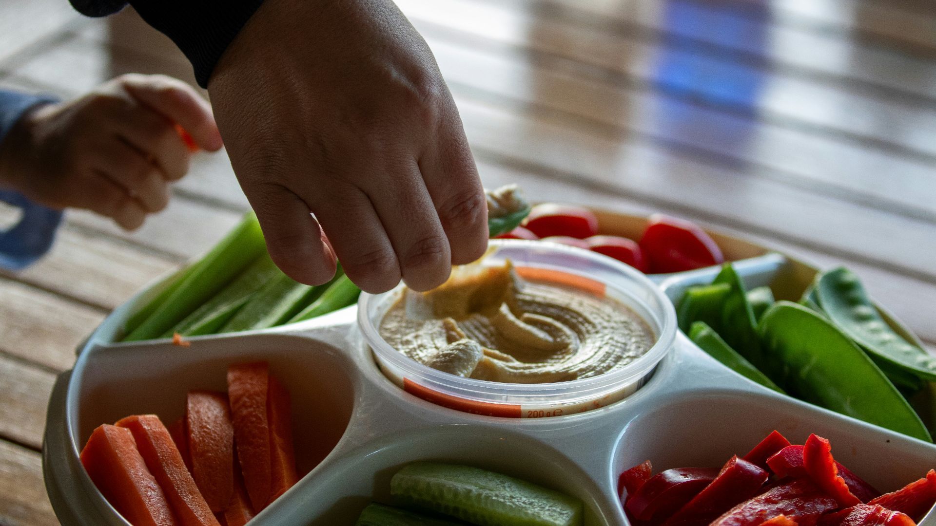 A person dipping dip into a bowl of vegetables