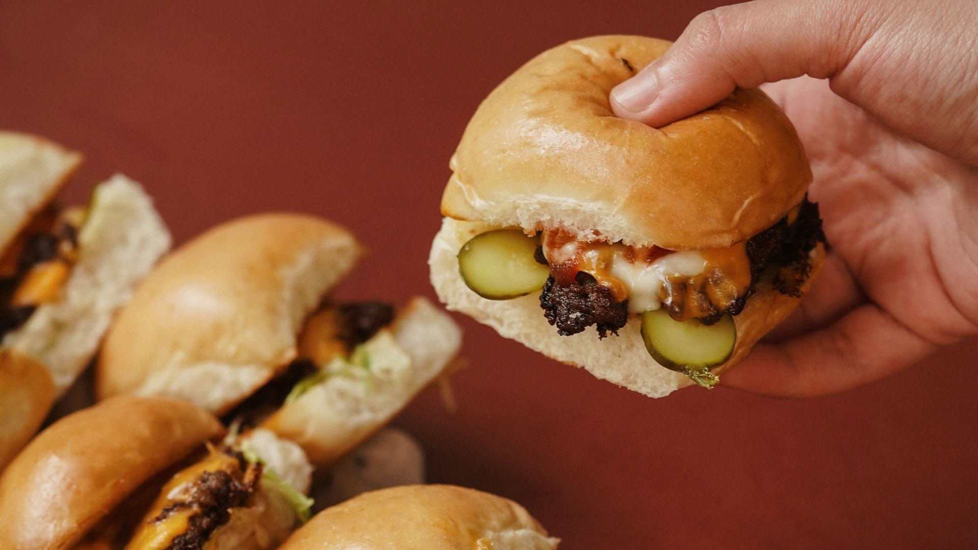 a hand holding a sandwich over a pile of mini sandwiches