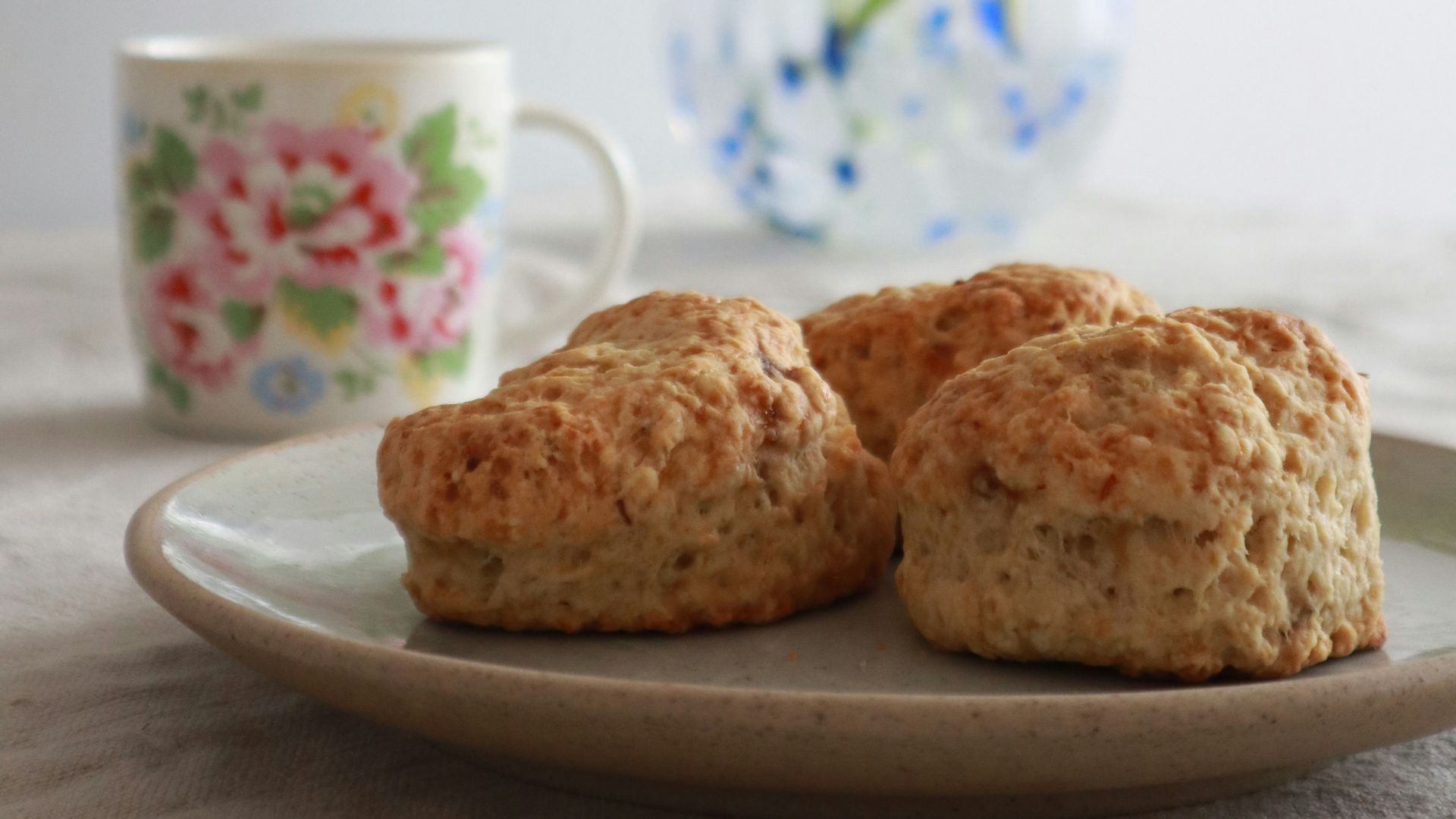 two biscuits on a plate next to a vase of flowers