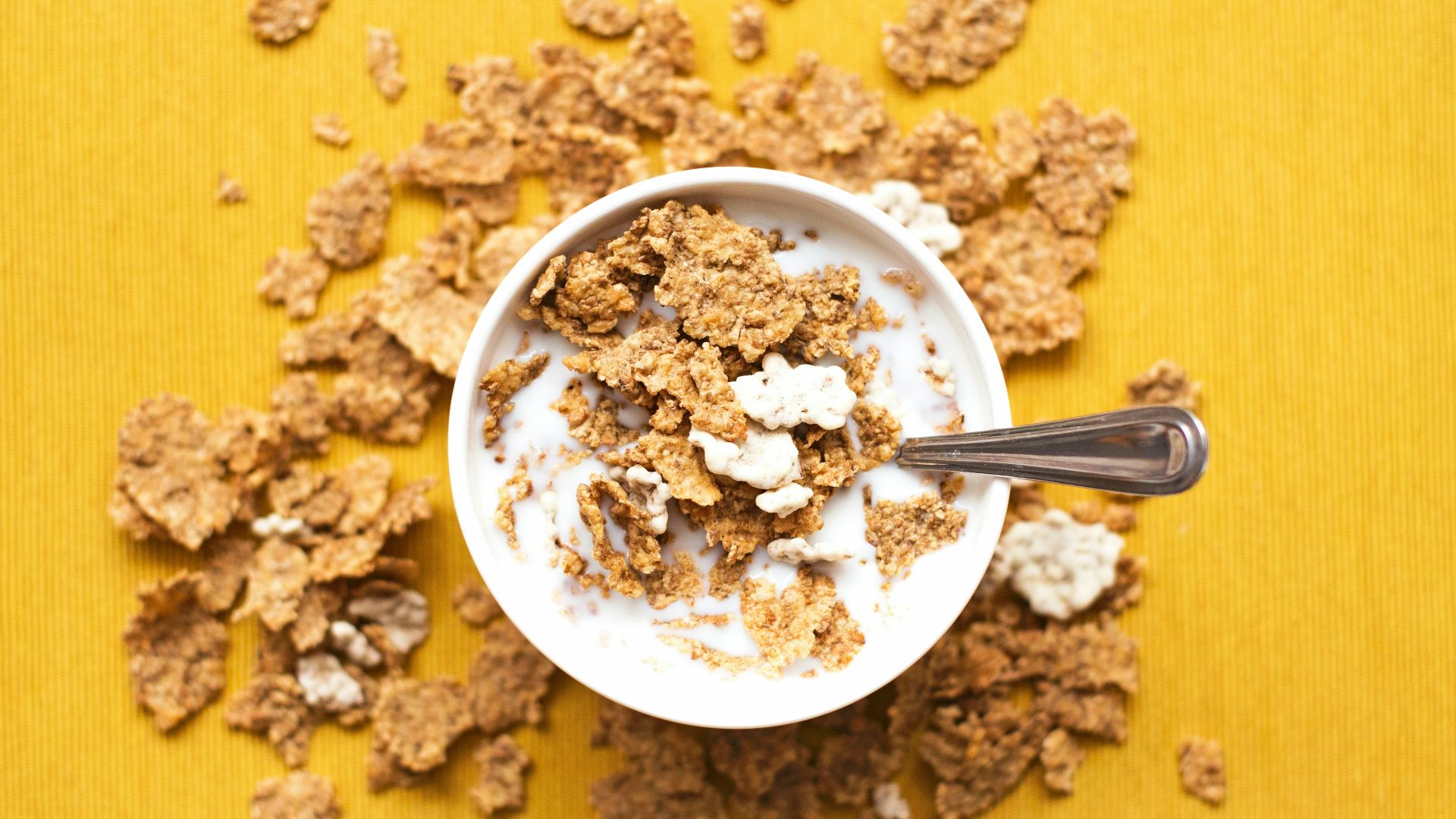 top view of corn flakes in bowl with milk and silver spoon