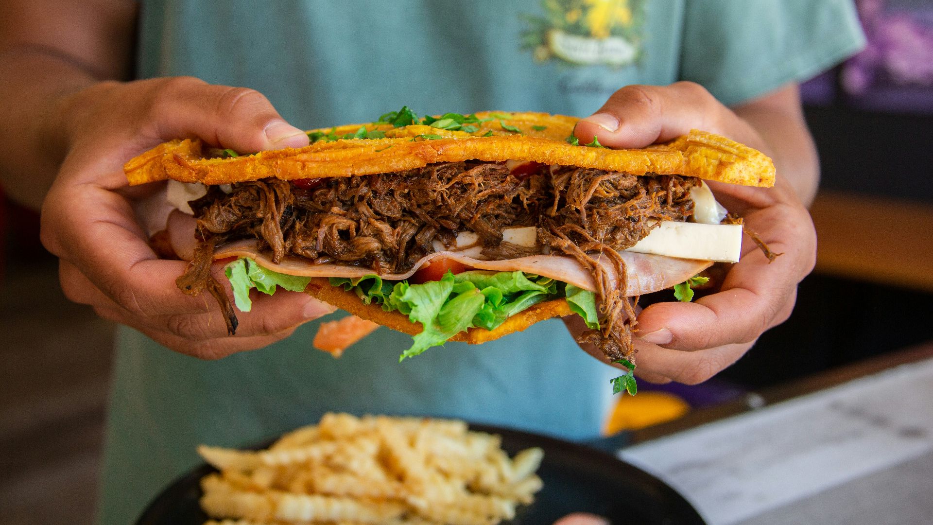a person holding a sandwich with meat and lettuce