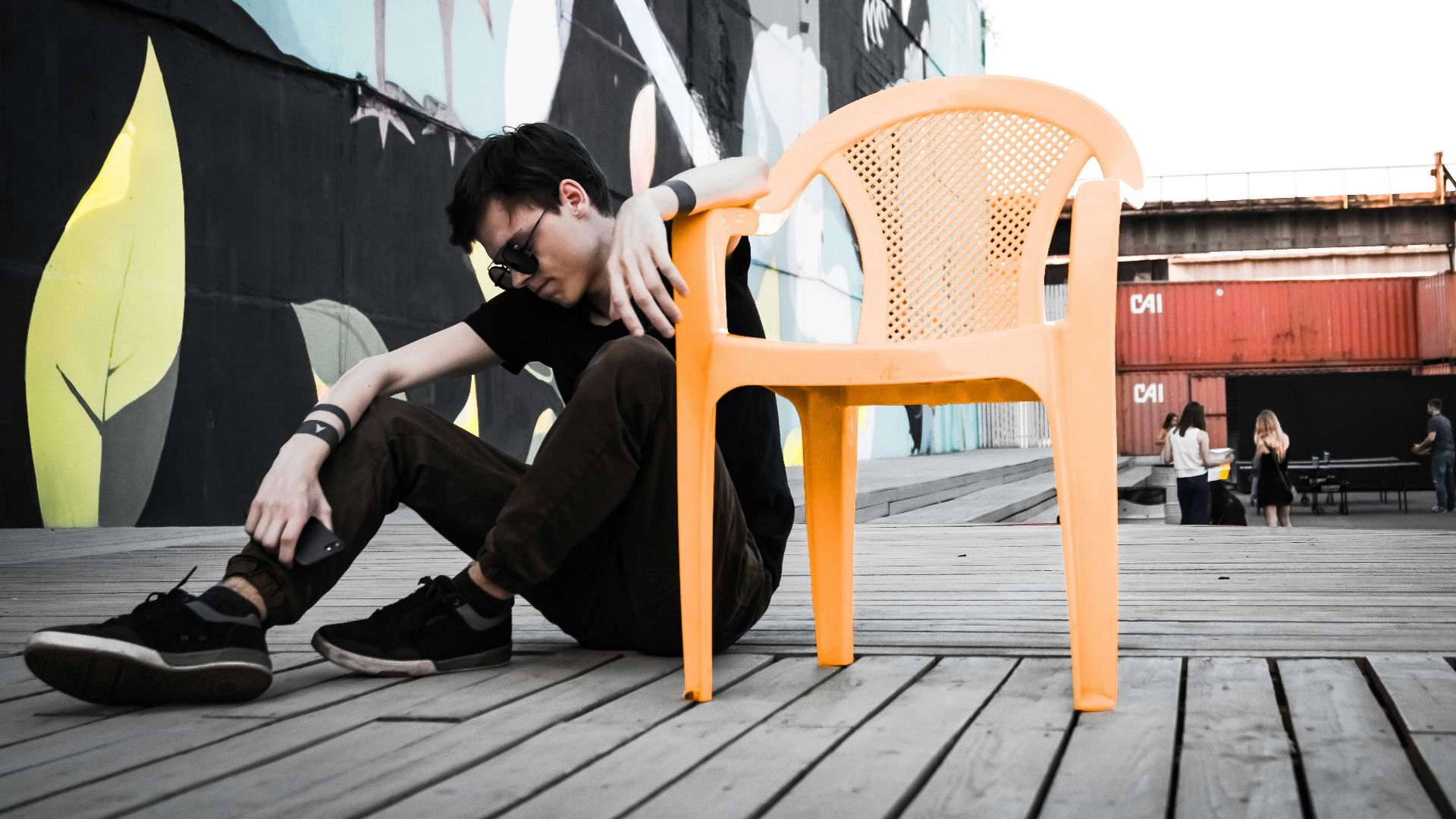 man sitting on floor beside empty orange plastic monobloc armchair at daytime