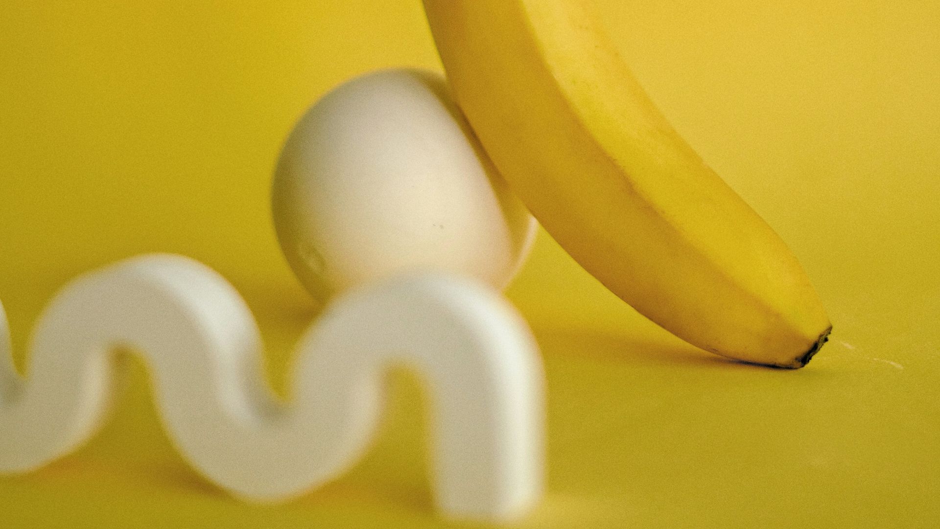a banana sitting next to an egg on a yellow background